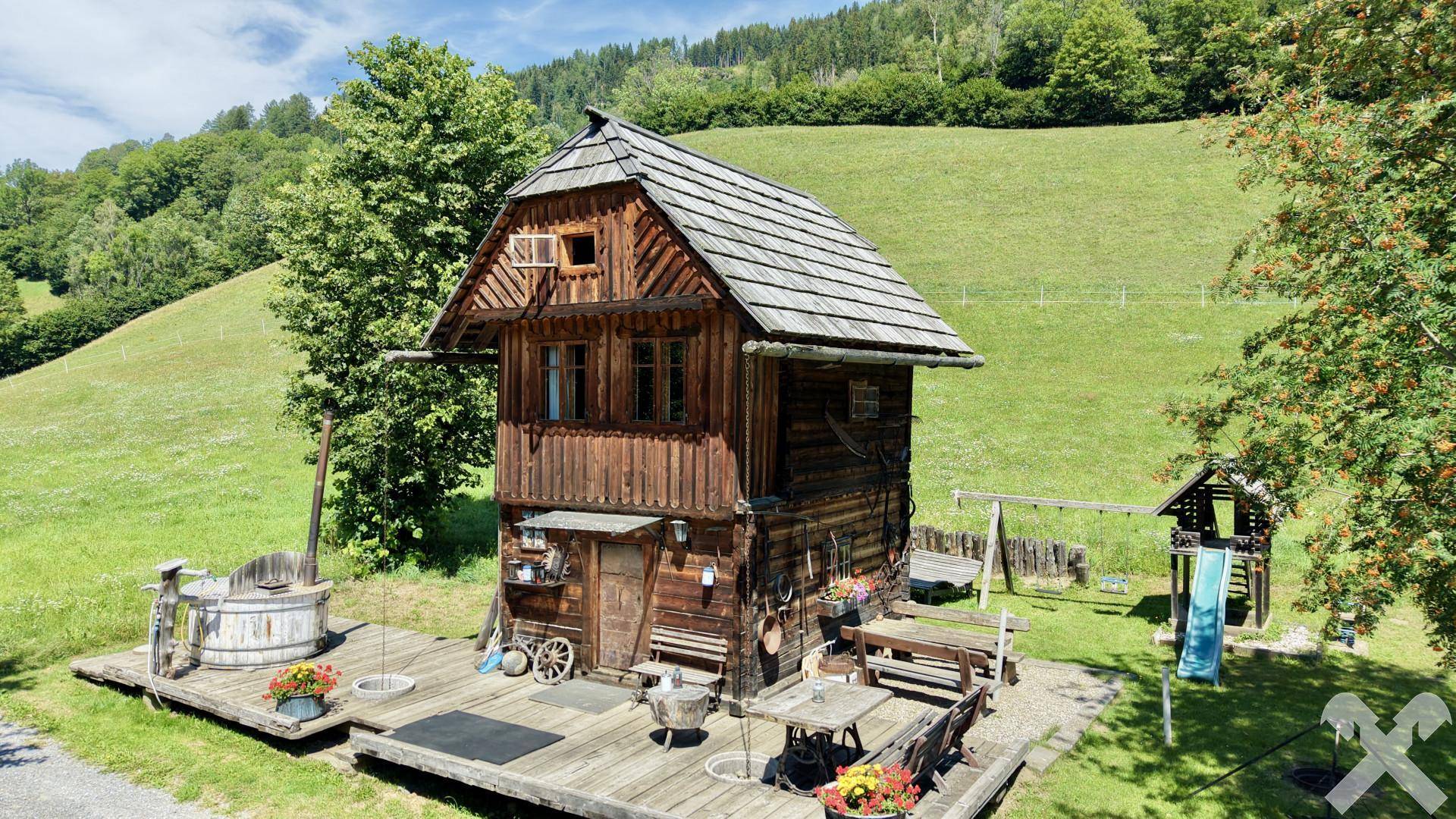 Kleines Holzhaus mit Holzdach, umgeben von einer Holzterrasse und einem Kinderspielplatz.