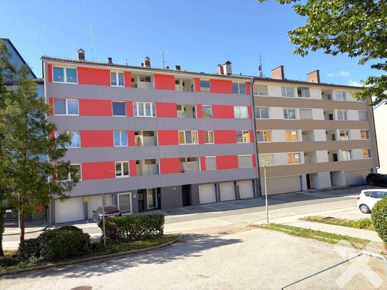 Ansicht von zwei Mehrfamilienhäusern mit farbigen Fassaden und Garagenzufahrten in grüner Umgebung.
