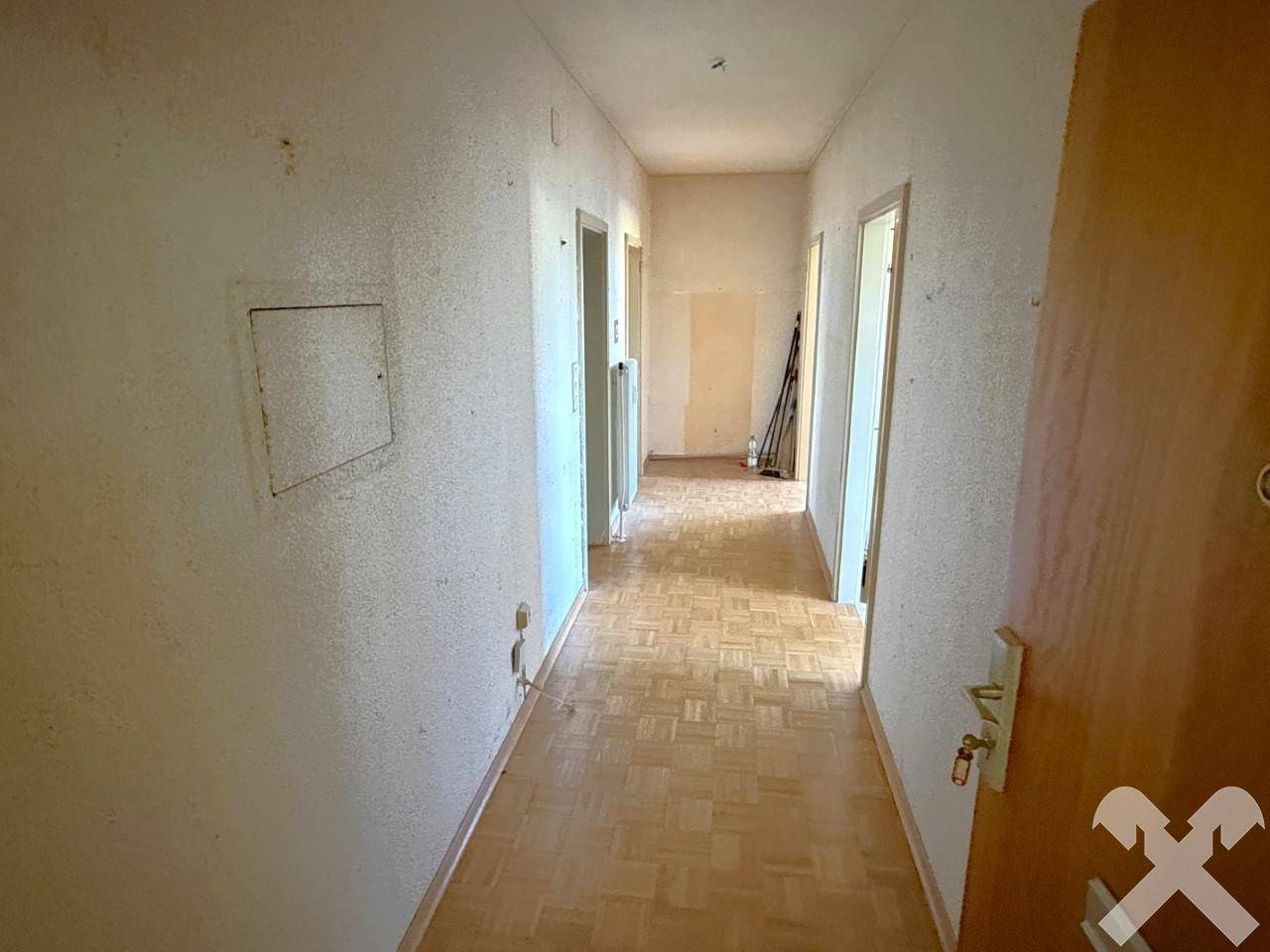 Langer Flur mit Parkettboden und mehreren Holztüren, der Renovierungsbedarf aufweist.