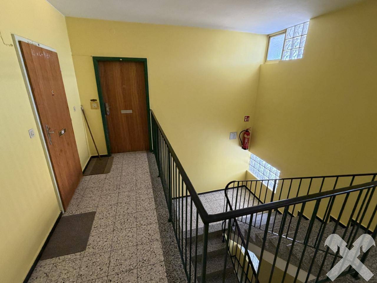 Helles Treppenhaus mit gelben Wänden, Terrazzoboden und einem robusten Metallgeländer.