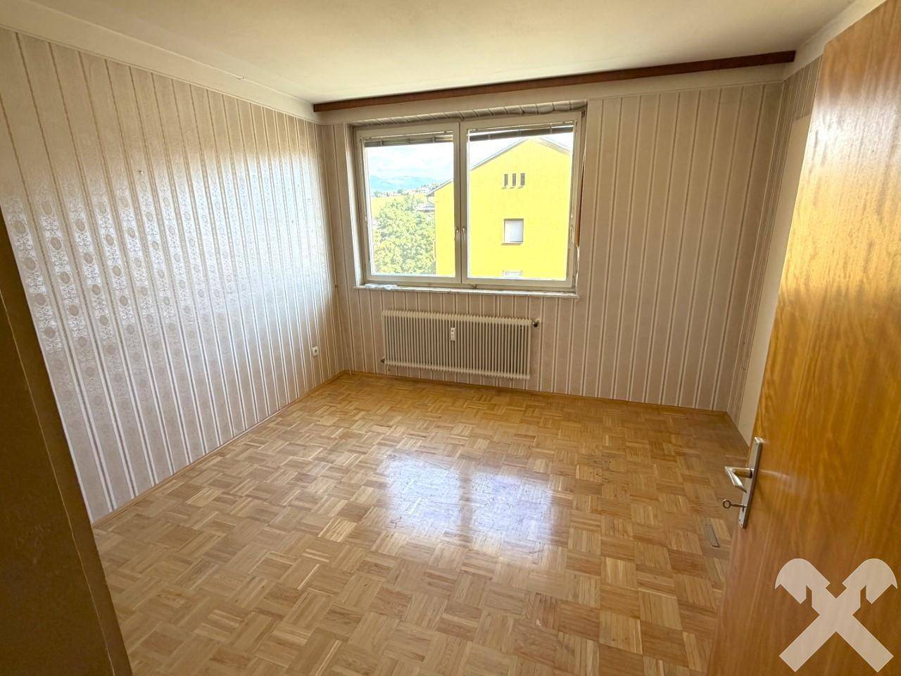Schlafzimmer mit Parkettboden, gestreifter Tapete und Fenster mit Blick ins Grüne.