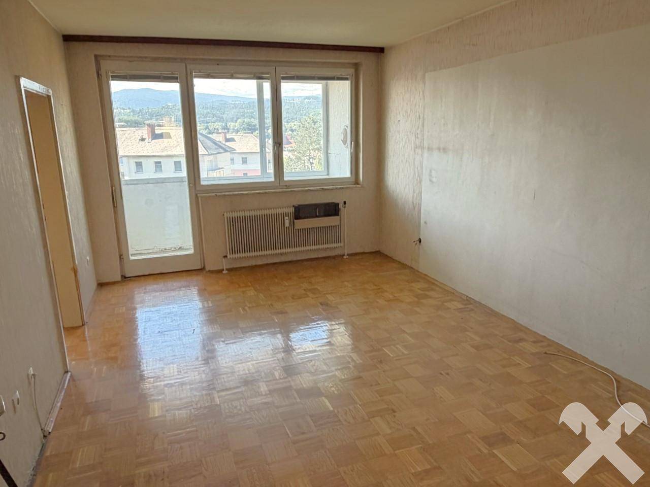 Geräumiges Wohnzimmer mit Parkettboden, Heizkörper und Zugang zu einem Balkon.