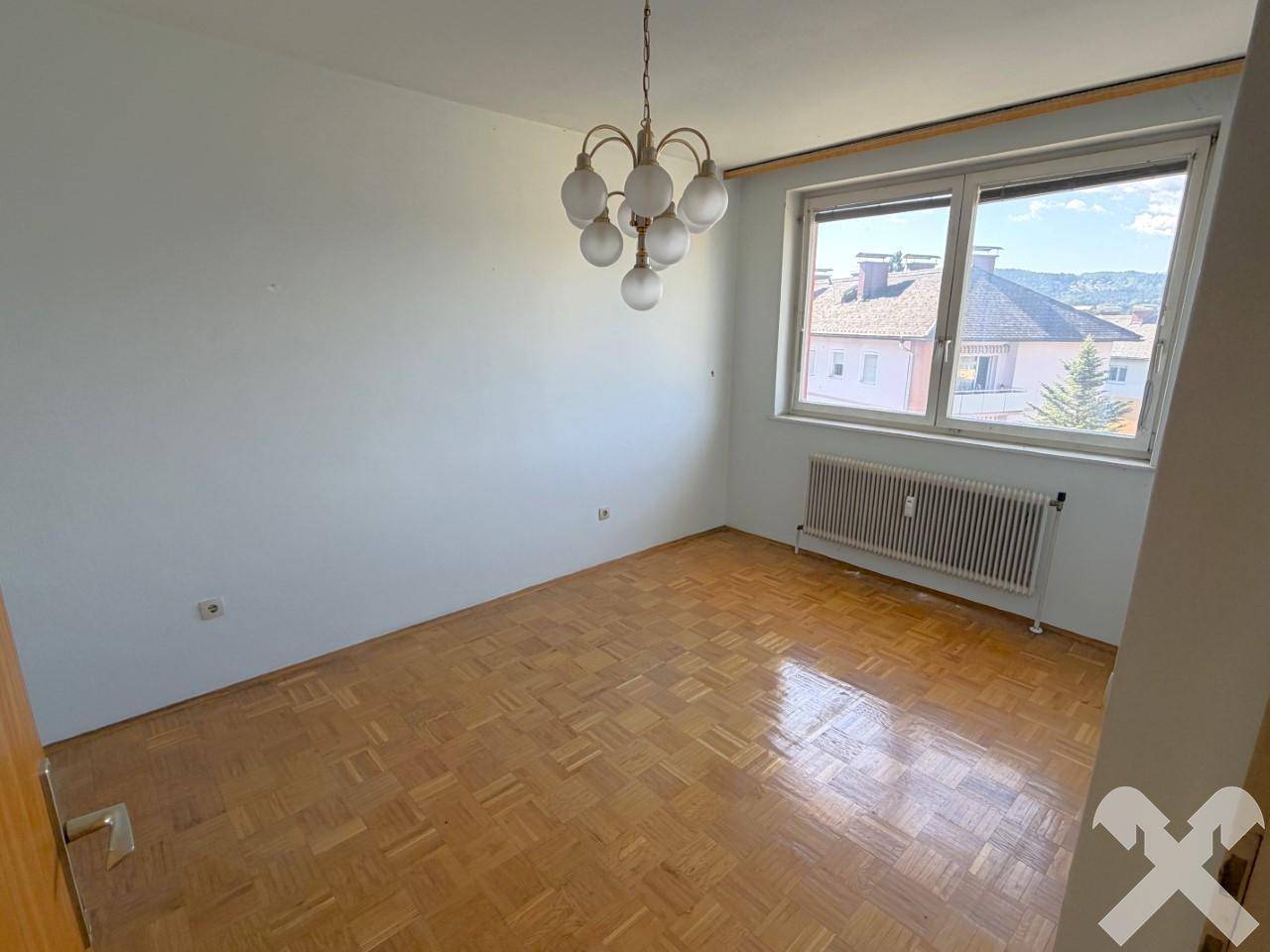 Schlafzimmer mit Parkettboden, großem Fenster und einer klassischen Deckenleuchte.