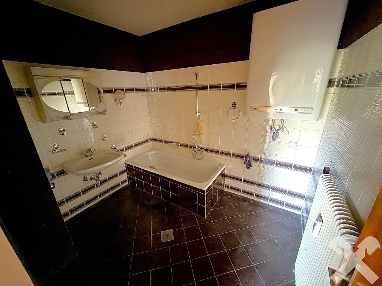 Badezimmer mit Badewanne, Waschbecken und Wandfliesen im Stil der 80er Jahre.