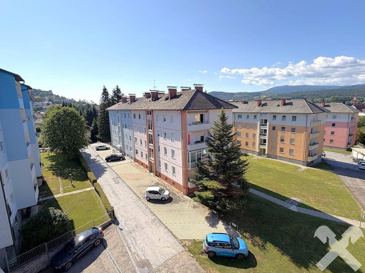 Weitläufige Ansicht von Wohngebäuden in einer grünen Umgebung mit Bergen im Hintergrund.