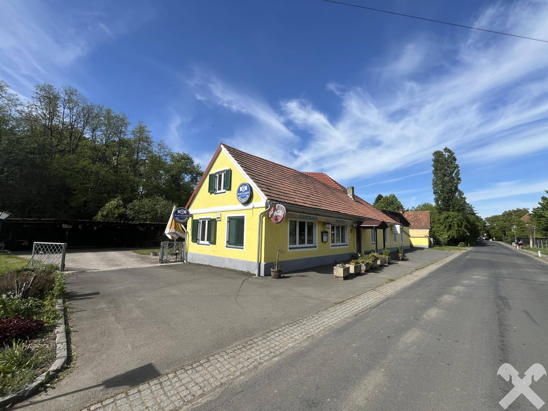 Ansicht des gelben Gebäudes mit rotem Dach und grünen Fensterläden von der Straßenseite.