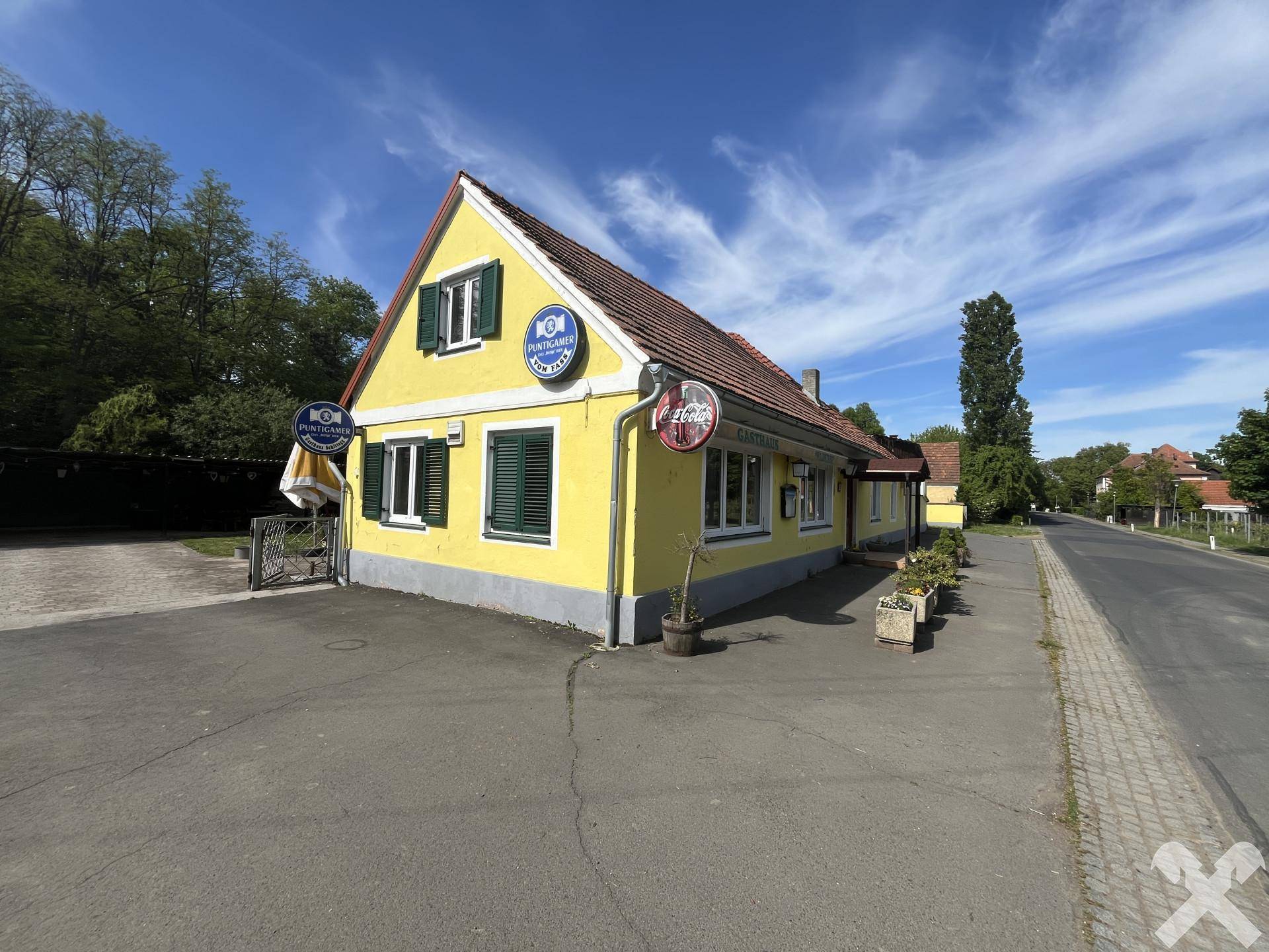 Gelbes Gebäude mit rotem Ziegeldach und grünen Fensterläden an einer Straße gelegen.