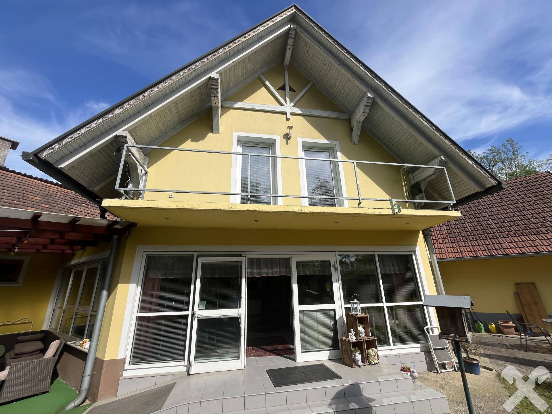 Fassade des gelben Gebäudes mit Balkon im Obergeschoss und großen Fenstertüren im Erdgeschoss.