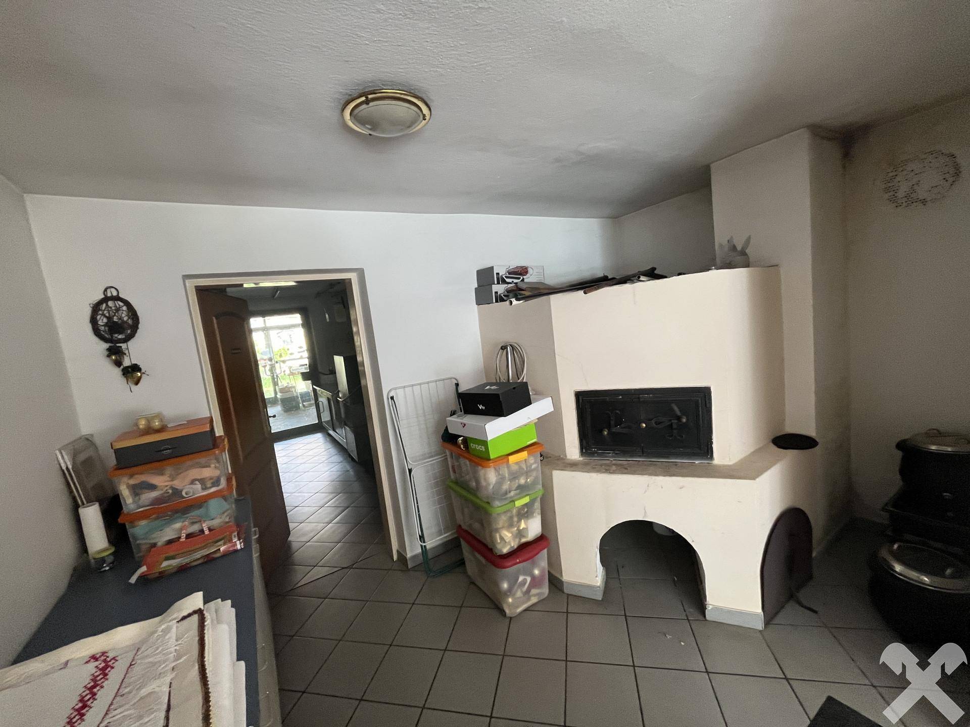 Raum mit einem großen gemauerten Kamin und Fliesenboden, der auf eine Küche führt.