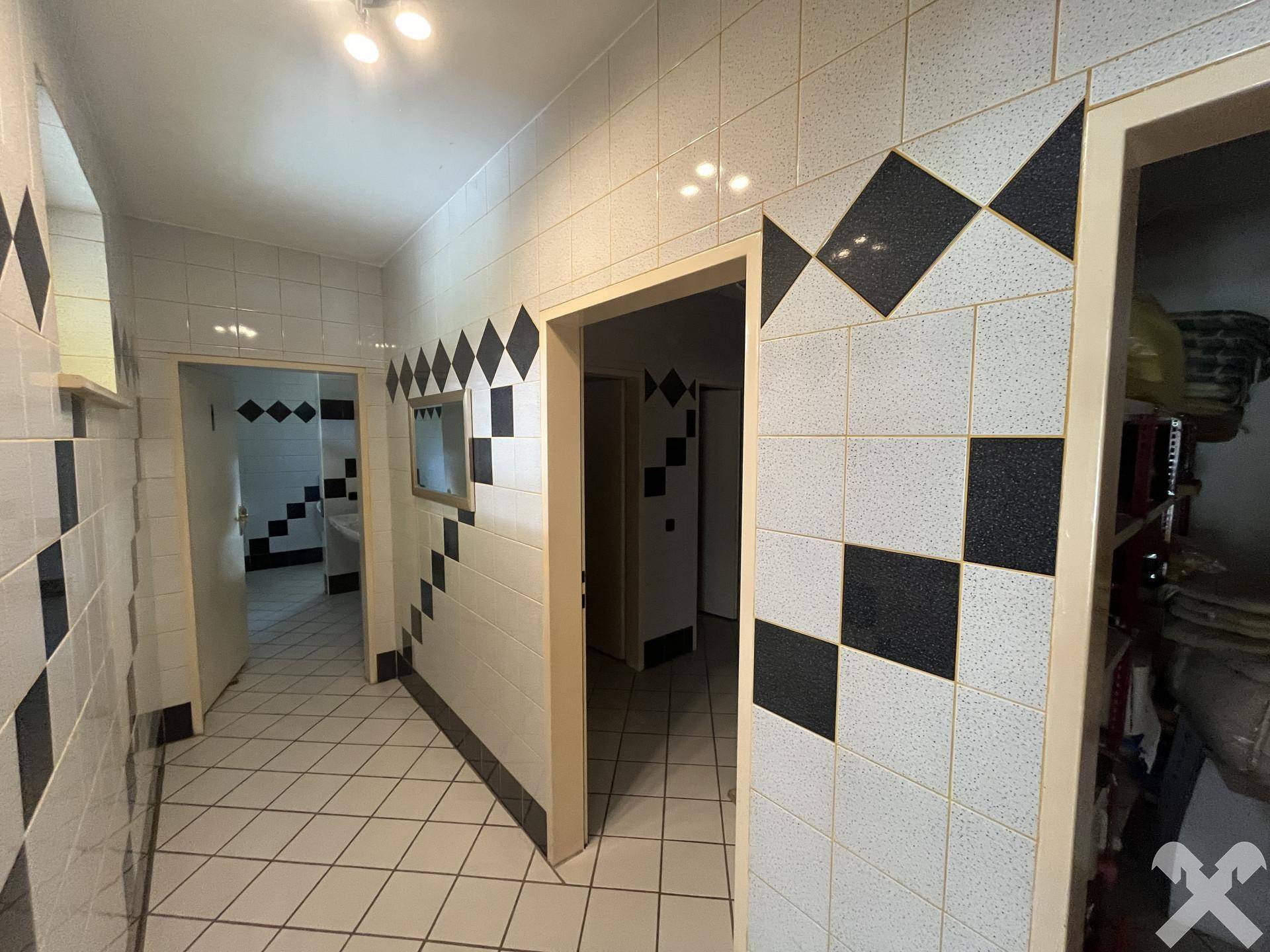 Flur mit schwarz-weiß gefliesten Wänden, der zu den Toilettenbereichen führt.