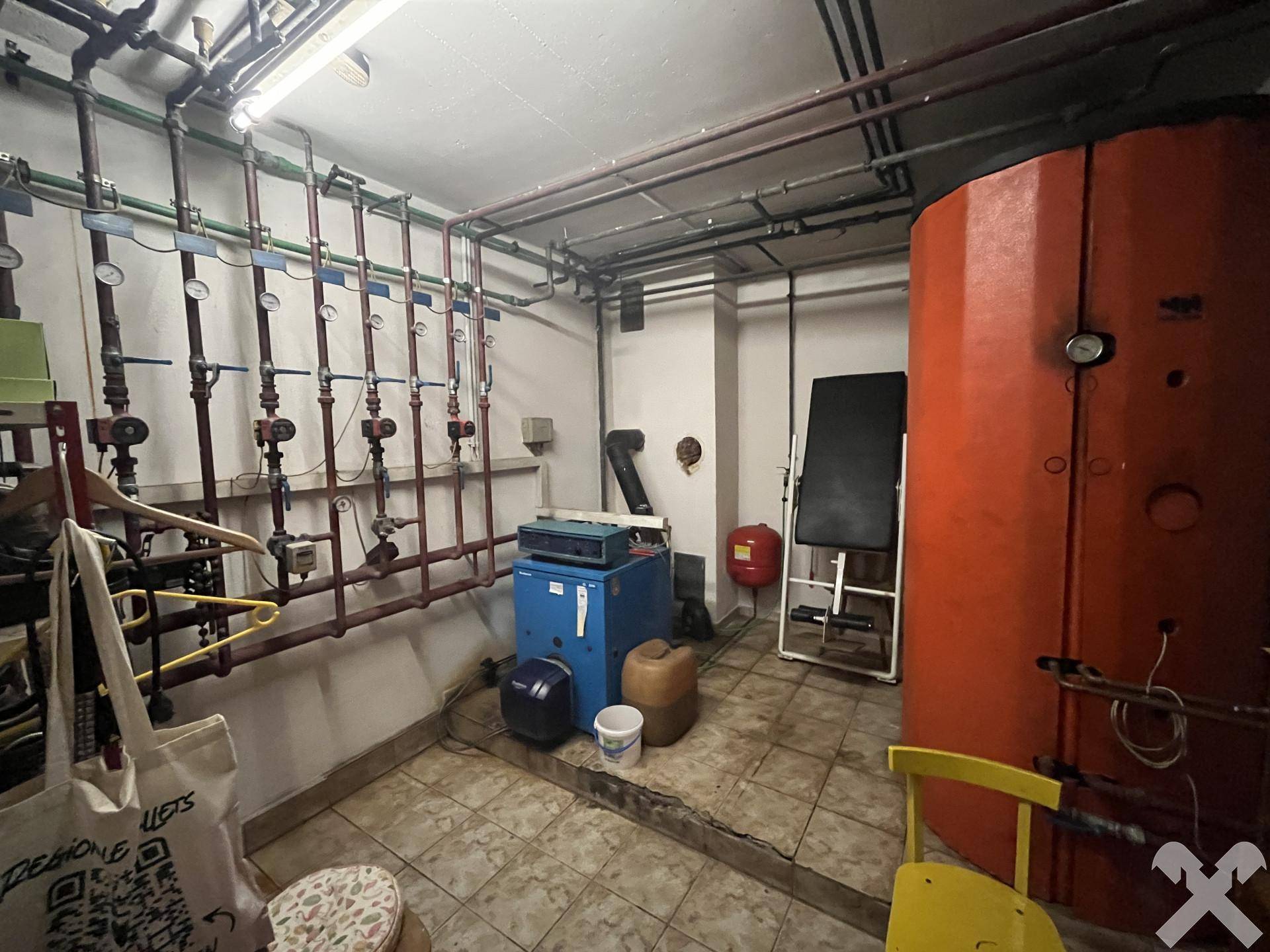 Heizungsraum mit großem Warmwasserspeicher, vielen Rohren und technischen Installationen.