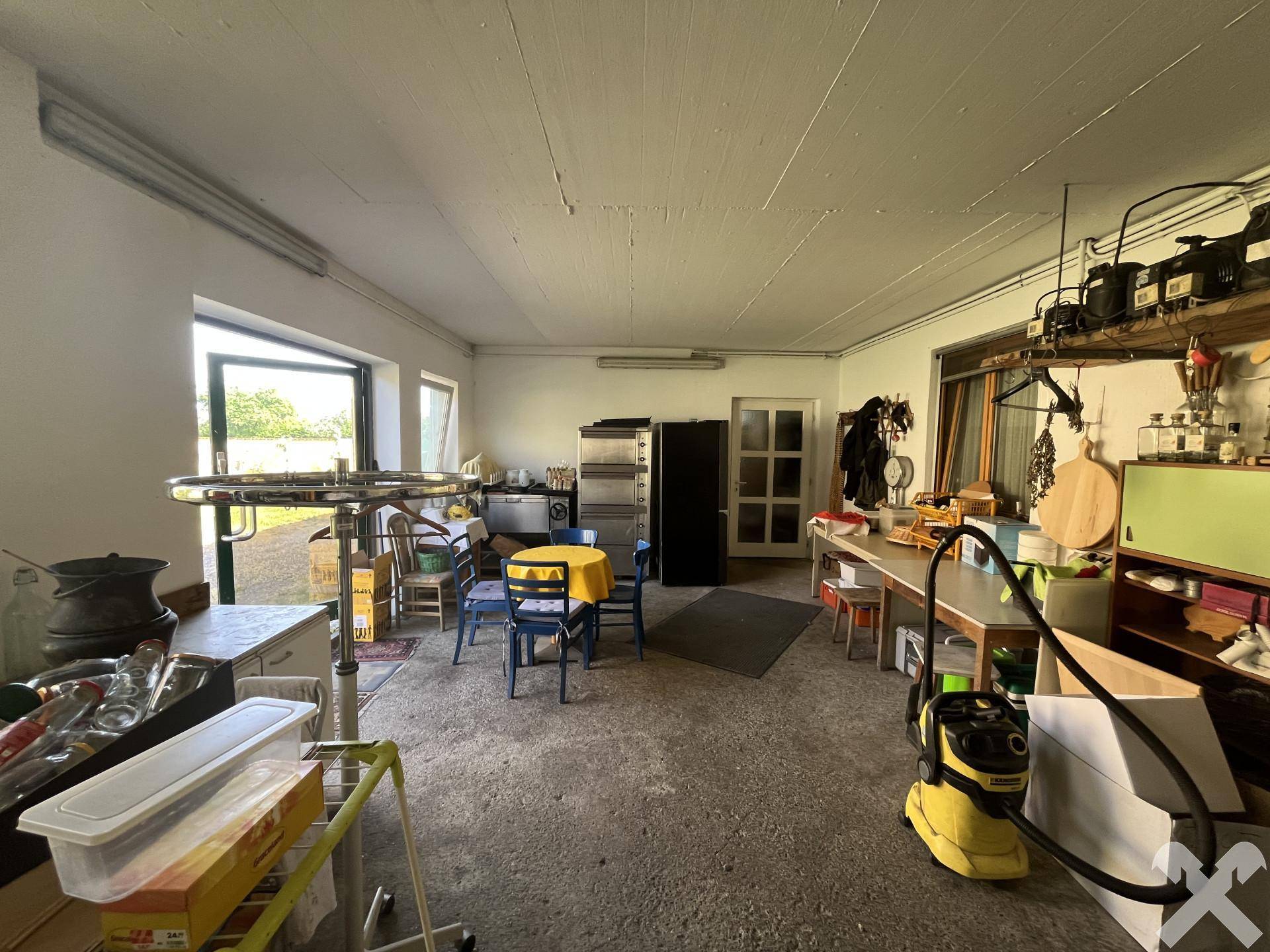 Großer Raum mit Betonboden, Fenstern und verschiedenen Gegenständen, der als Werkstatt oder Abstellraum genutzt wird.