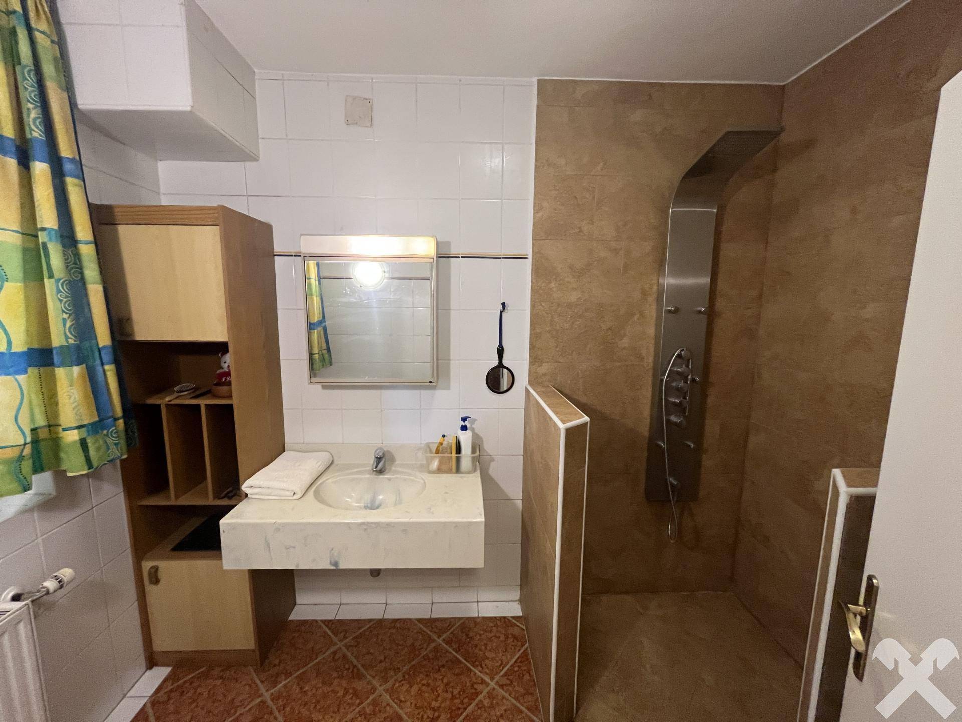 Badezimmer mit Duschkabine, Waschbecken und gefliesten Wänden in Braun- und Beigetönen.
