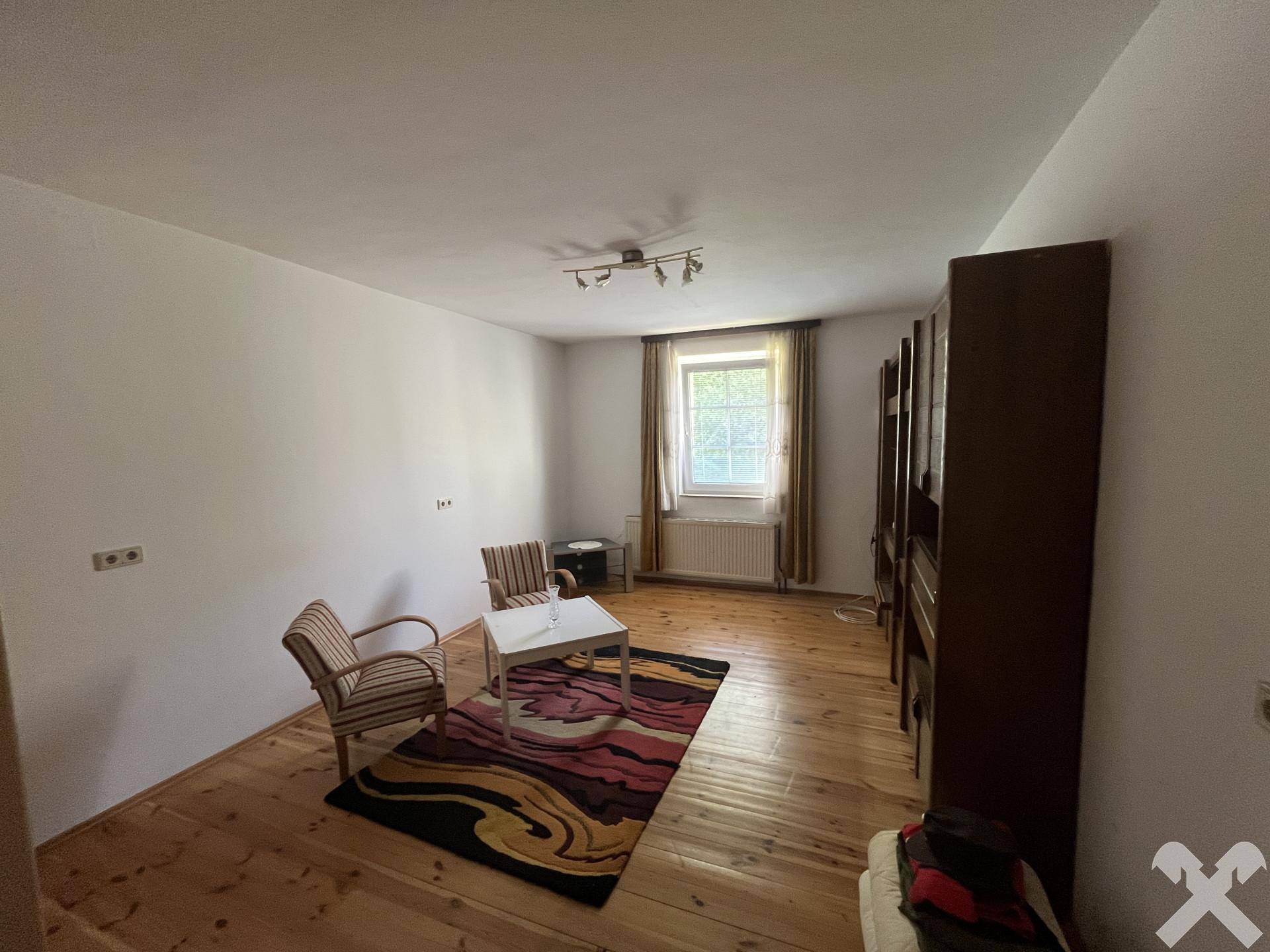 Helles Schlafzimmer mit Holzdielenboden, einem Fenster und einfacher Möblierung.