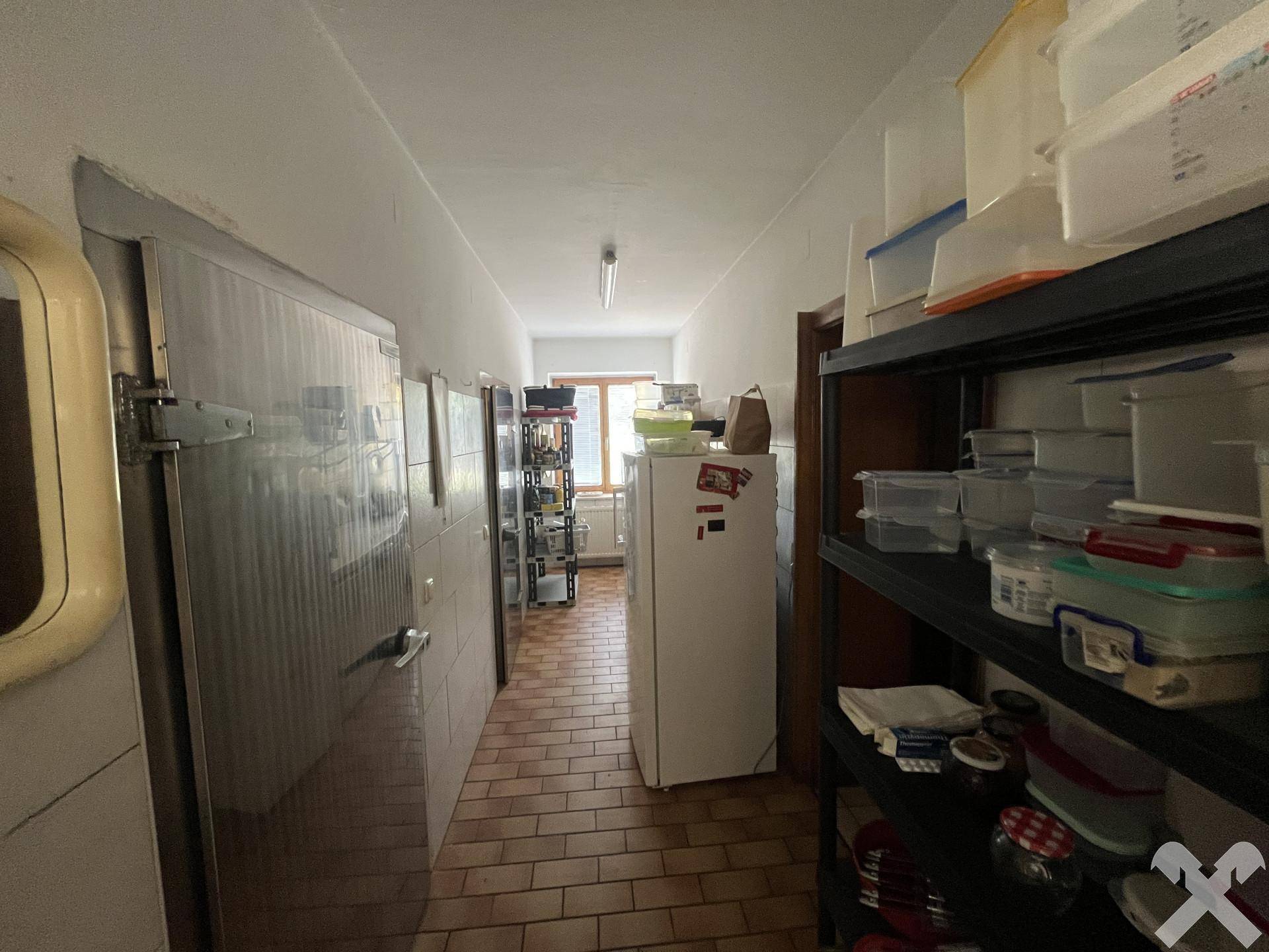 Lagerraum mit mehreren Kühlschränken und Regalen für Vorräte, gefliestem Boden.