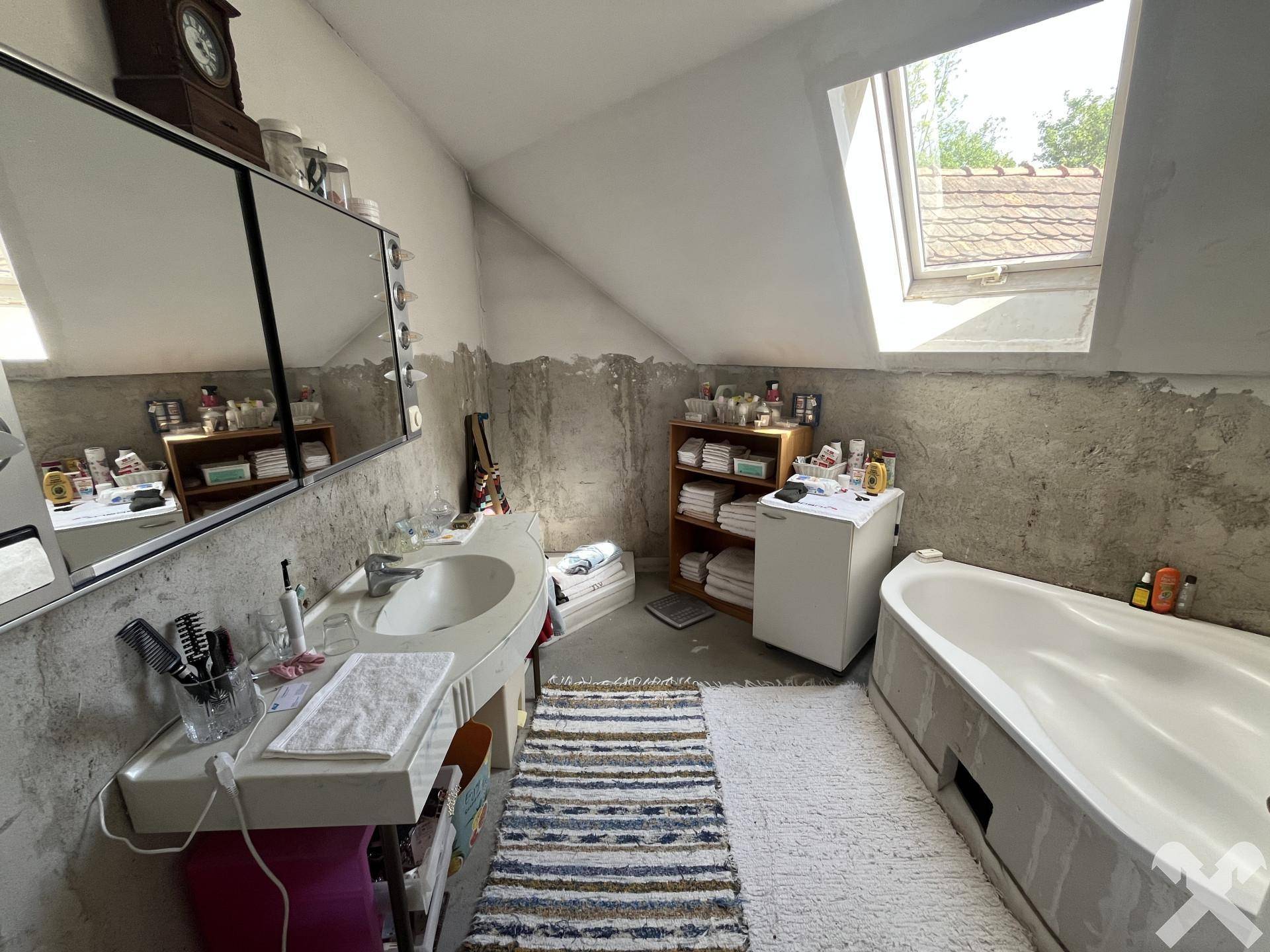 Badezimmer im Dachgeschoss mit Badewanne, Waschbecken und Dachfenster, das noch unfertig wirkt.