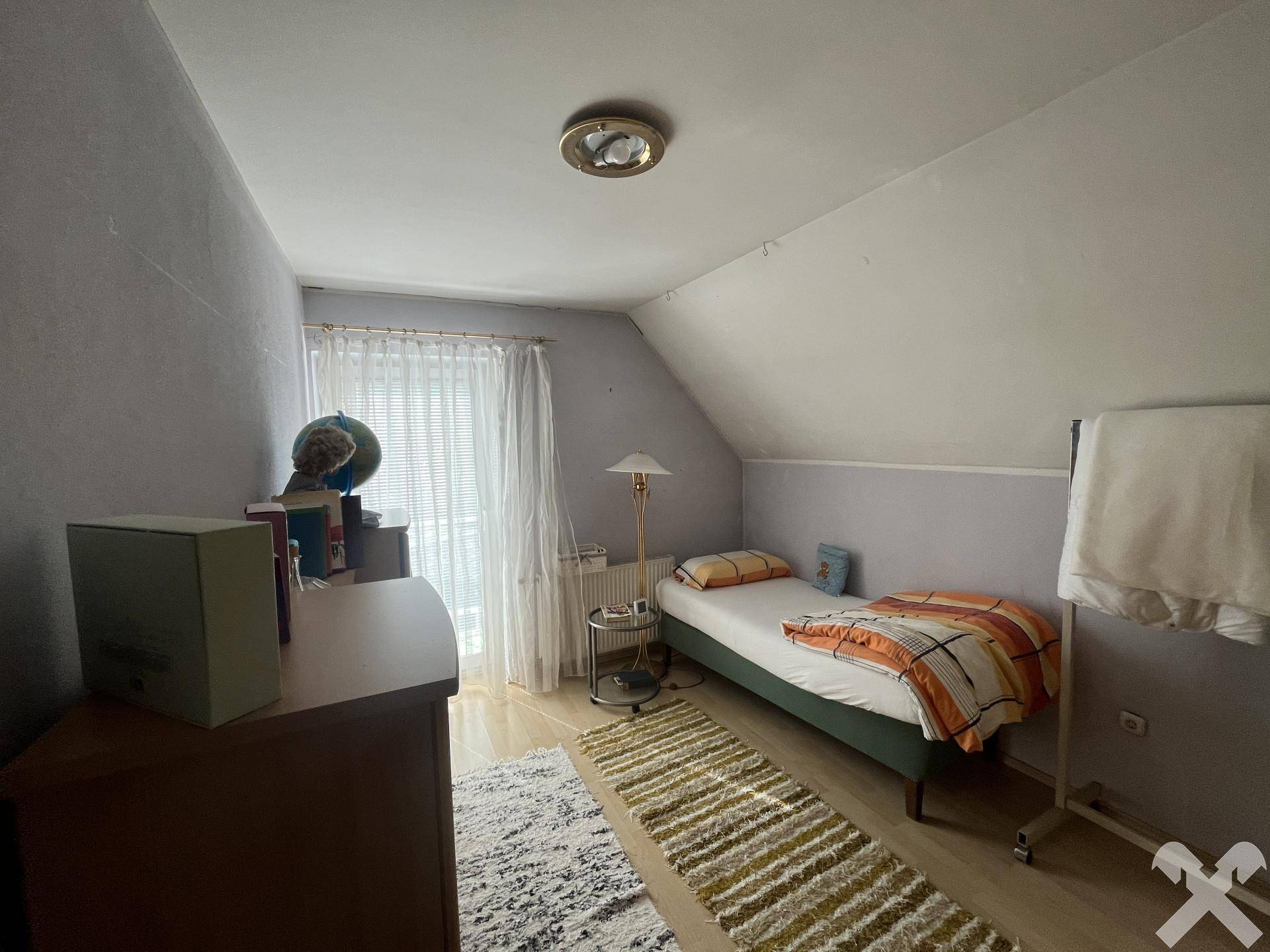 Helles Schlafzimmer mit Einzelbett, Schreibtisch und Dachschräge, das einen gemütlichen Rückzugsort bietet.