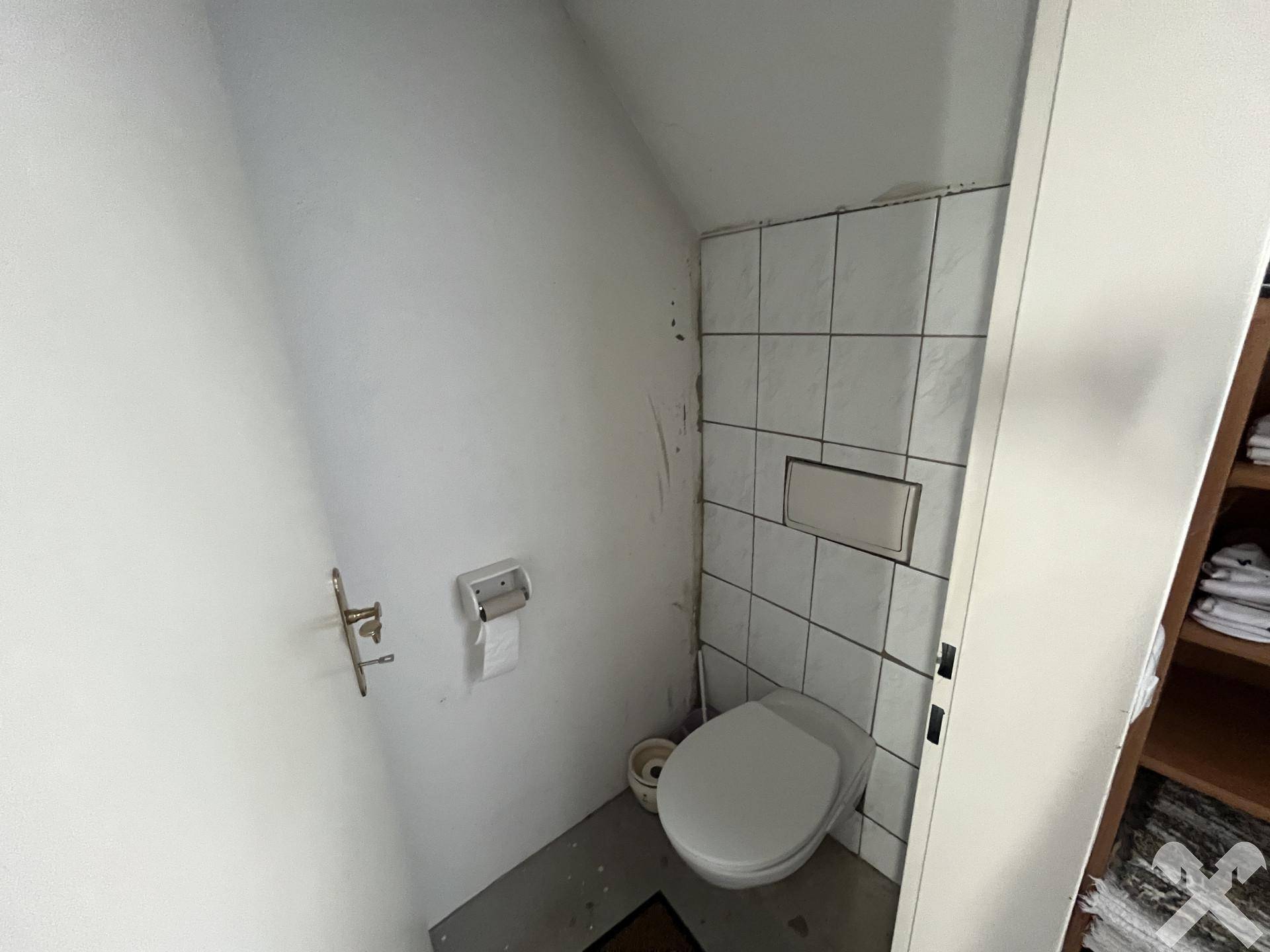 Kleines Gäste-WC mit Wand-WC und Fliesen an der Wand, das funktional und einfach gehalten ist.