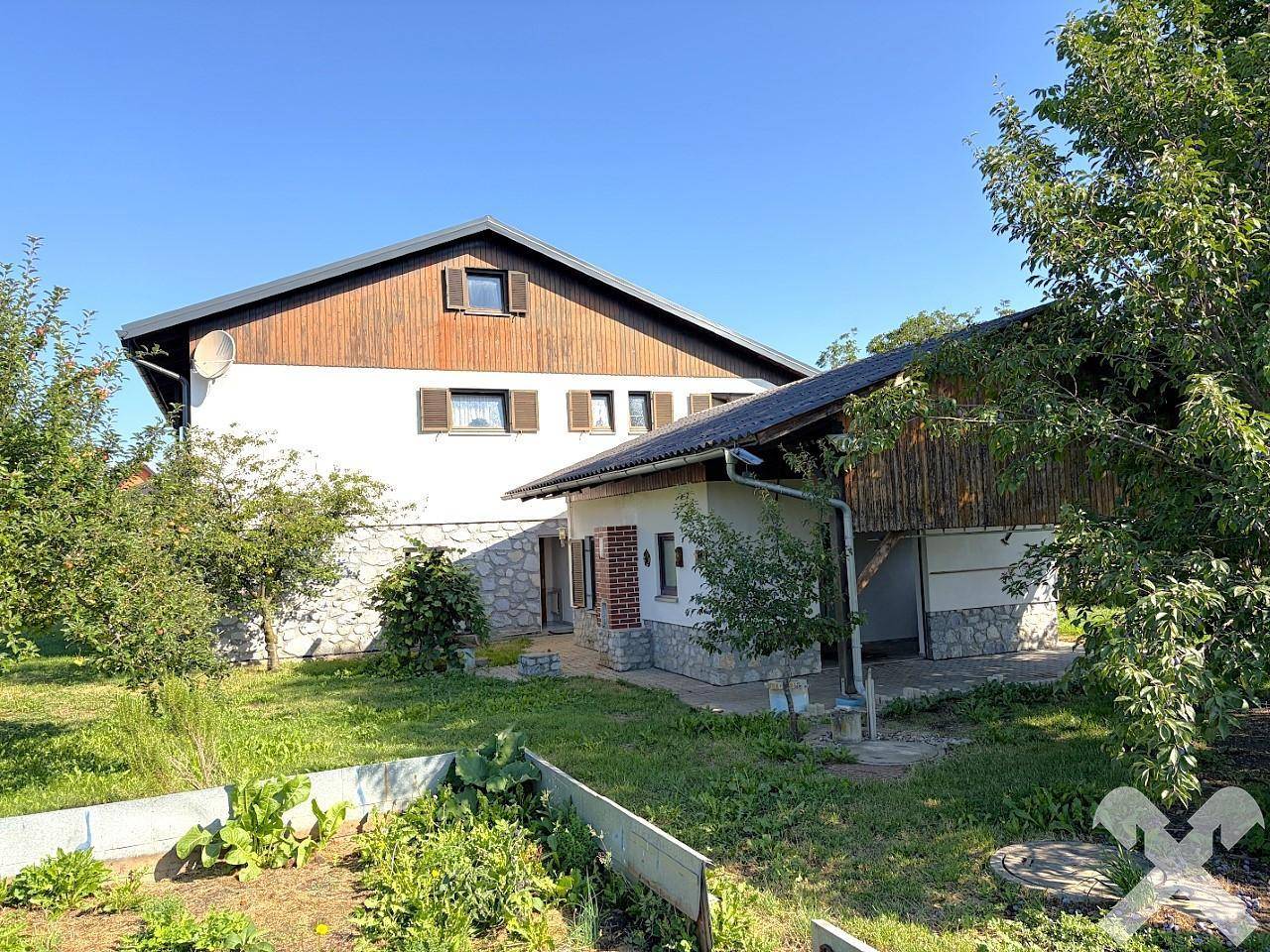 Rückansicht des Hauses mit Gemüsegarten und angrenzendem Anbau unter blauem Himmel.