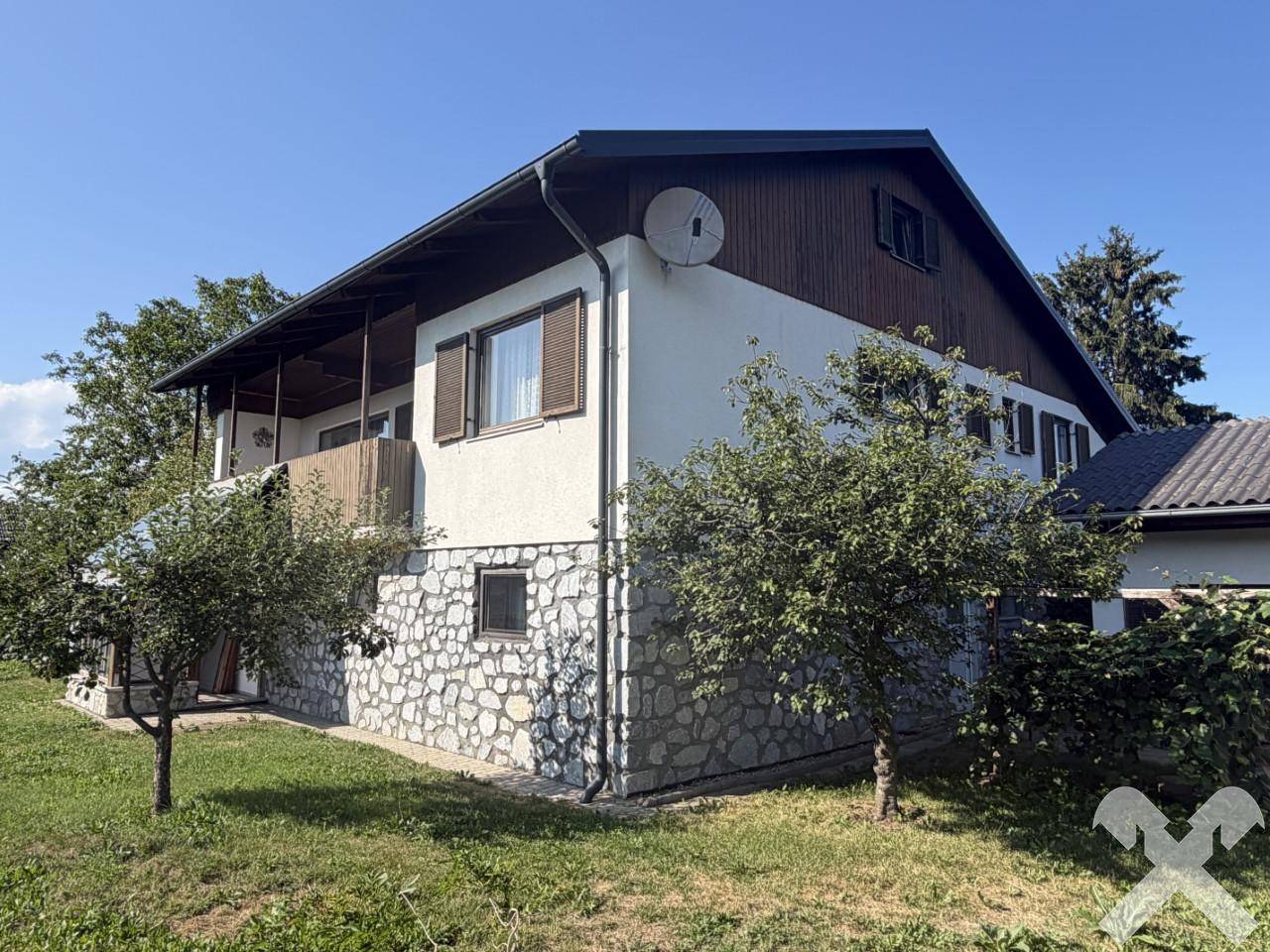Seitenansicht des Hauses mit Holzbalkon und Satellitenschüssel unter blauem Himmel.