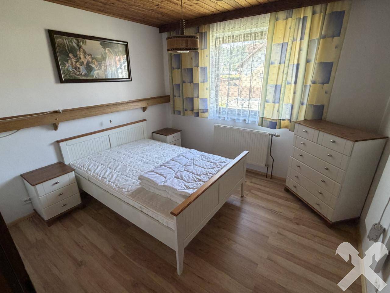 Helles Schlafzimmer mit Doppelbett, Holzmöbeln und Fenster mit Vorhängen.