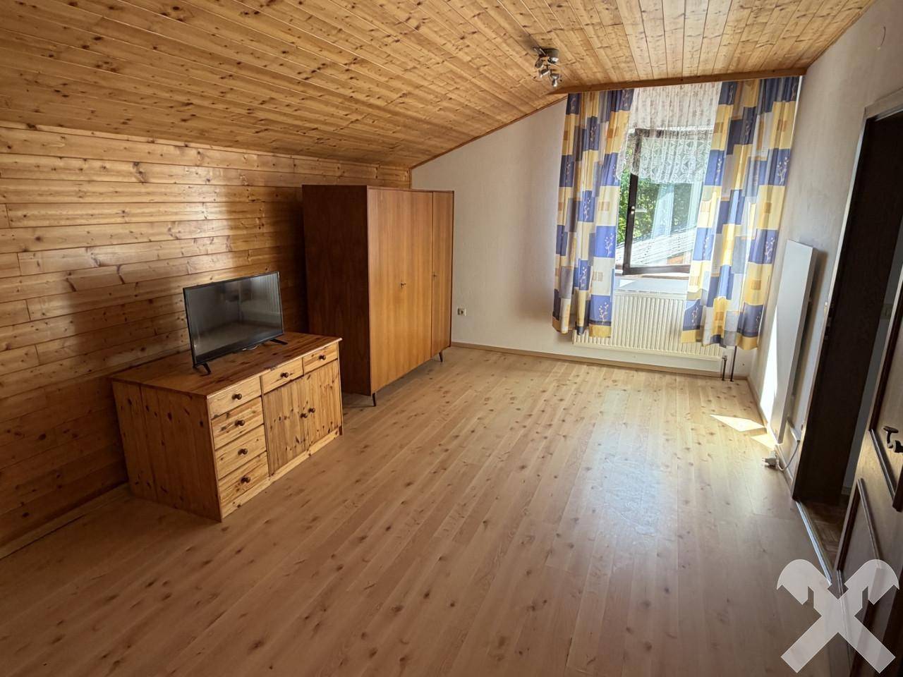Schlafzimmer mit Holzvertäfelung, Holzboden und Fenster mit Blick ins Grüne.