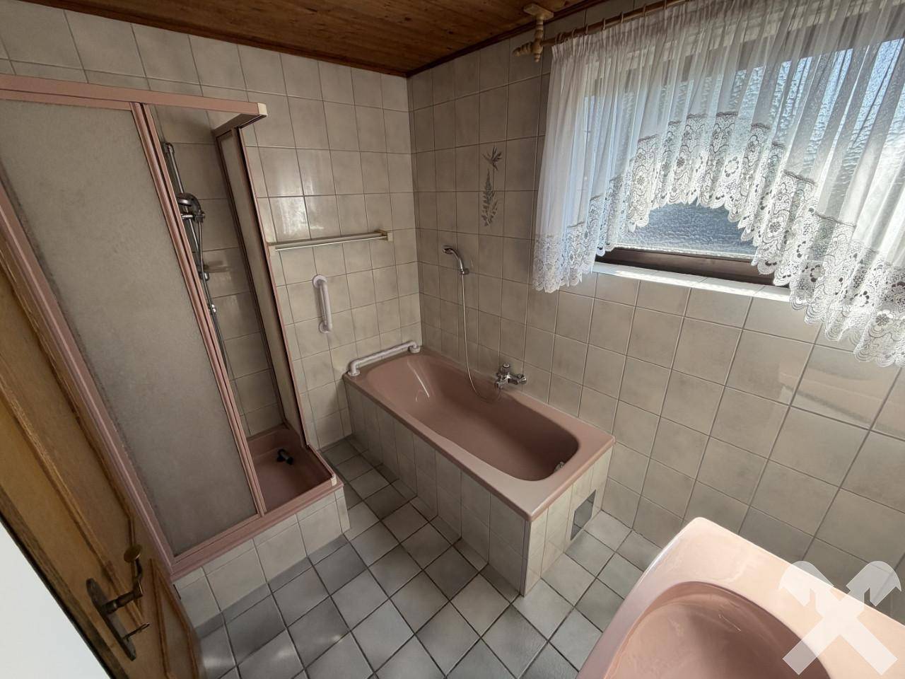 Badezimmer im 80er-Jahre-Stil mit rosa Badewanne, Dusche und hellen Fliesen.