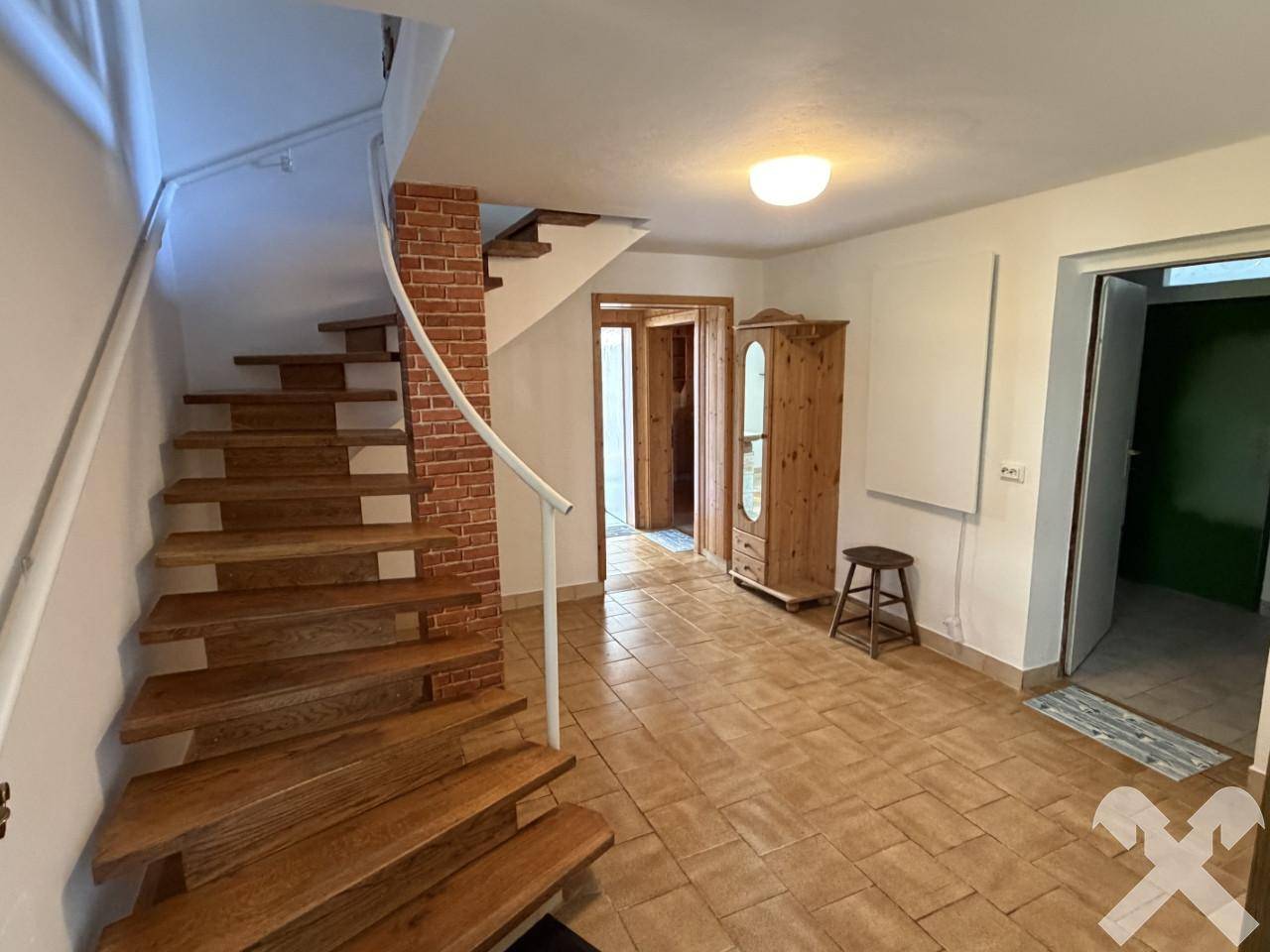 Heller Eingangsbereich mit Holztreppe, Fliesenboden und rustikalem Schrank.