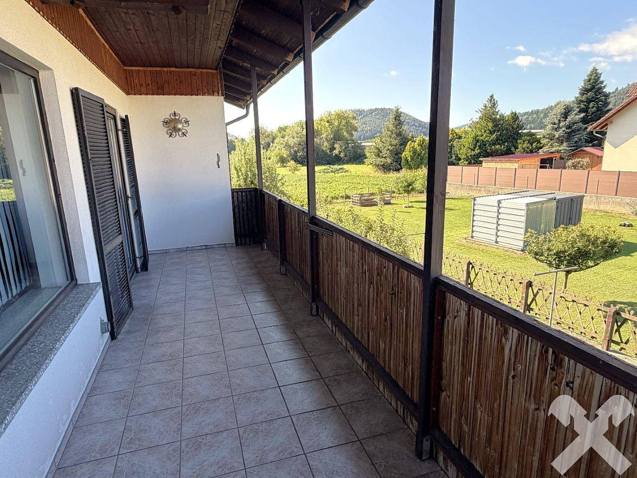 Langer Balkon mit Fliesenboden, Holzgeländer und weitem Blick ins Grüne.