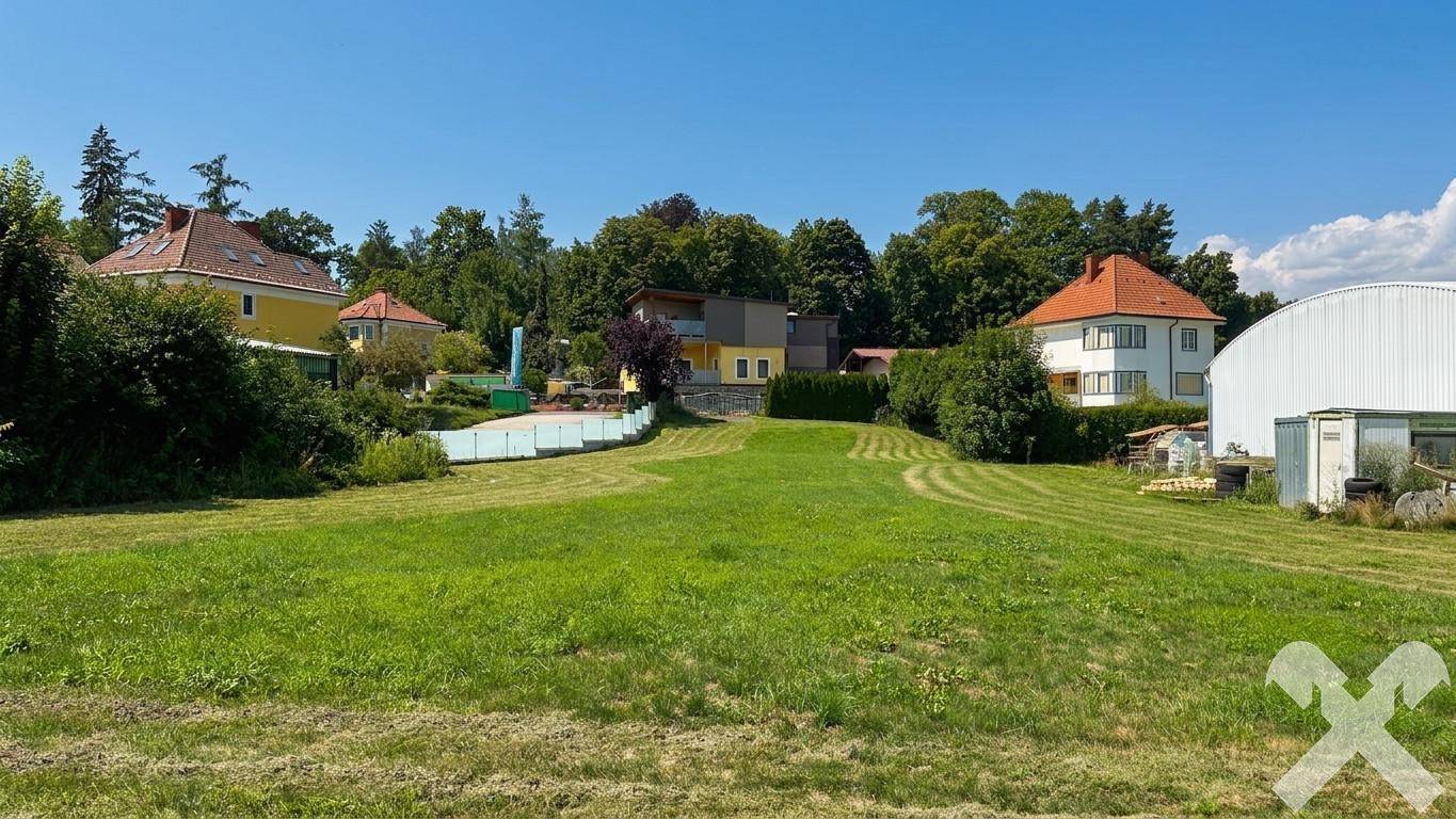 Große, gepflegte Grünfläche mit mehreren Wohnhäusern und Bäumen im Hintergrund unter blauem Himmel.