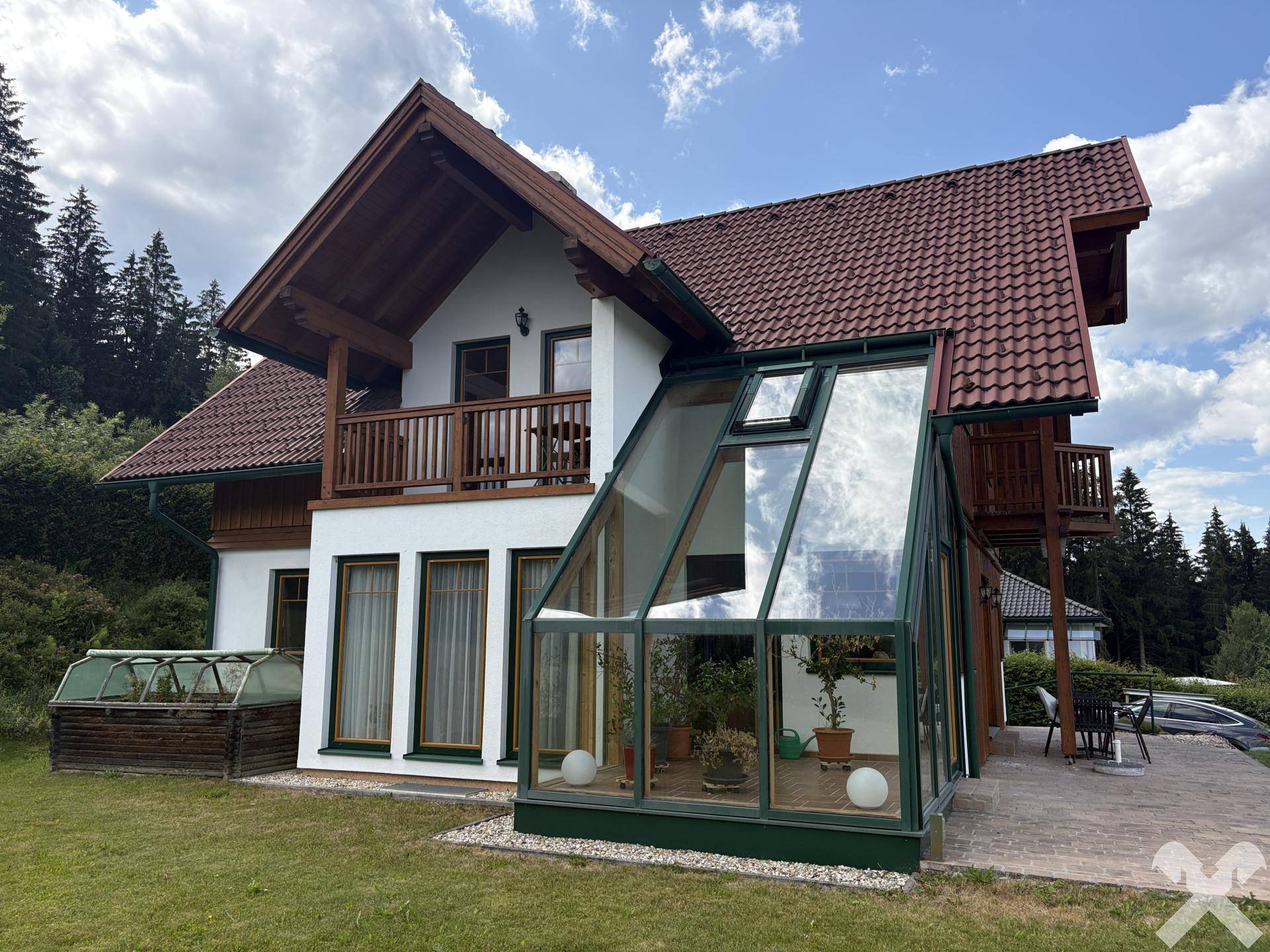 Außenansicht des Hauses mit Wintergarten, kleinem Gewächshaus und gepflastertem Bereich.