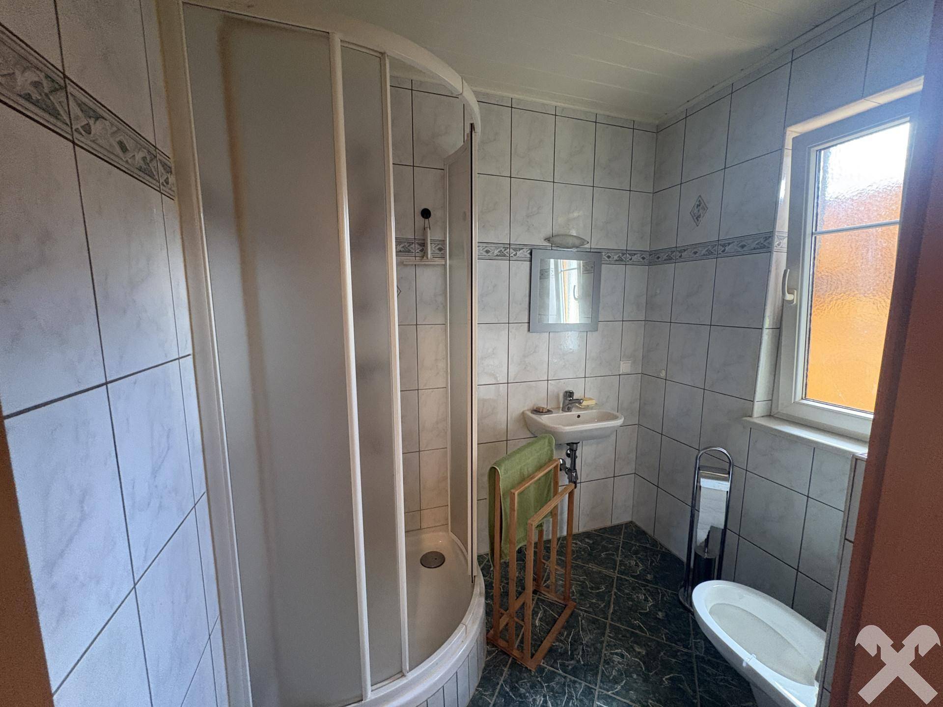 Kleines Badezimmer mit grünen Fliesen, Duschkabine, Waschbecken und Toilette.