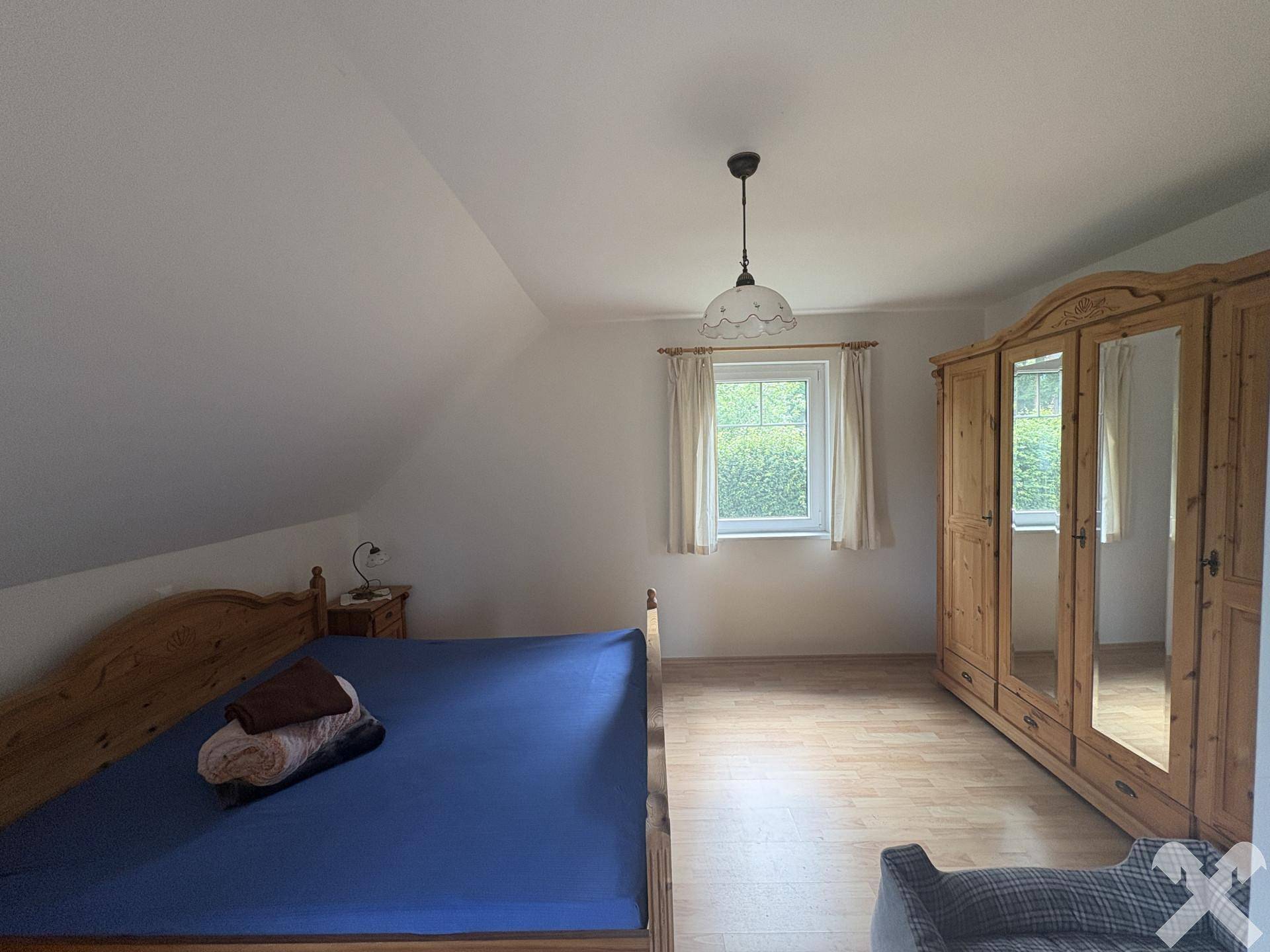 Schlafzimmer mit Holzbett, großem Spiegelschrank und Laminatboden unter Dachschräge.