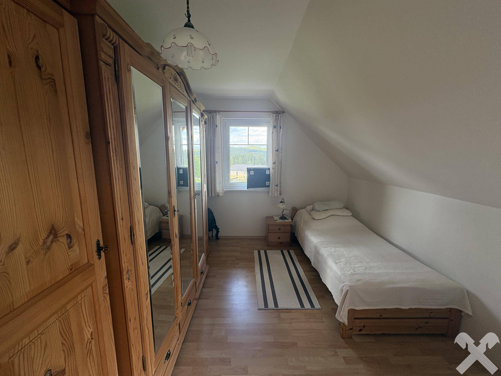 Helles Schlafzimmer mit Einzelbett, Spiegelschrank und Laminatboden unter Dachschräge.
