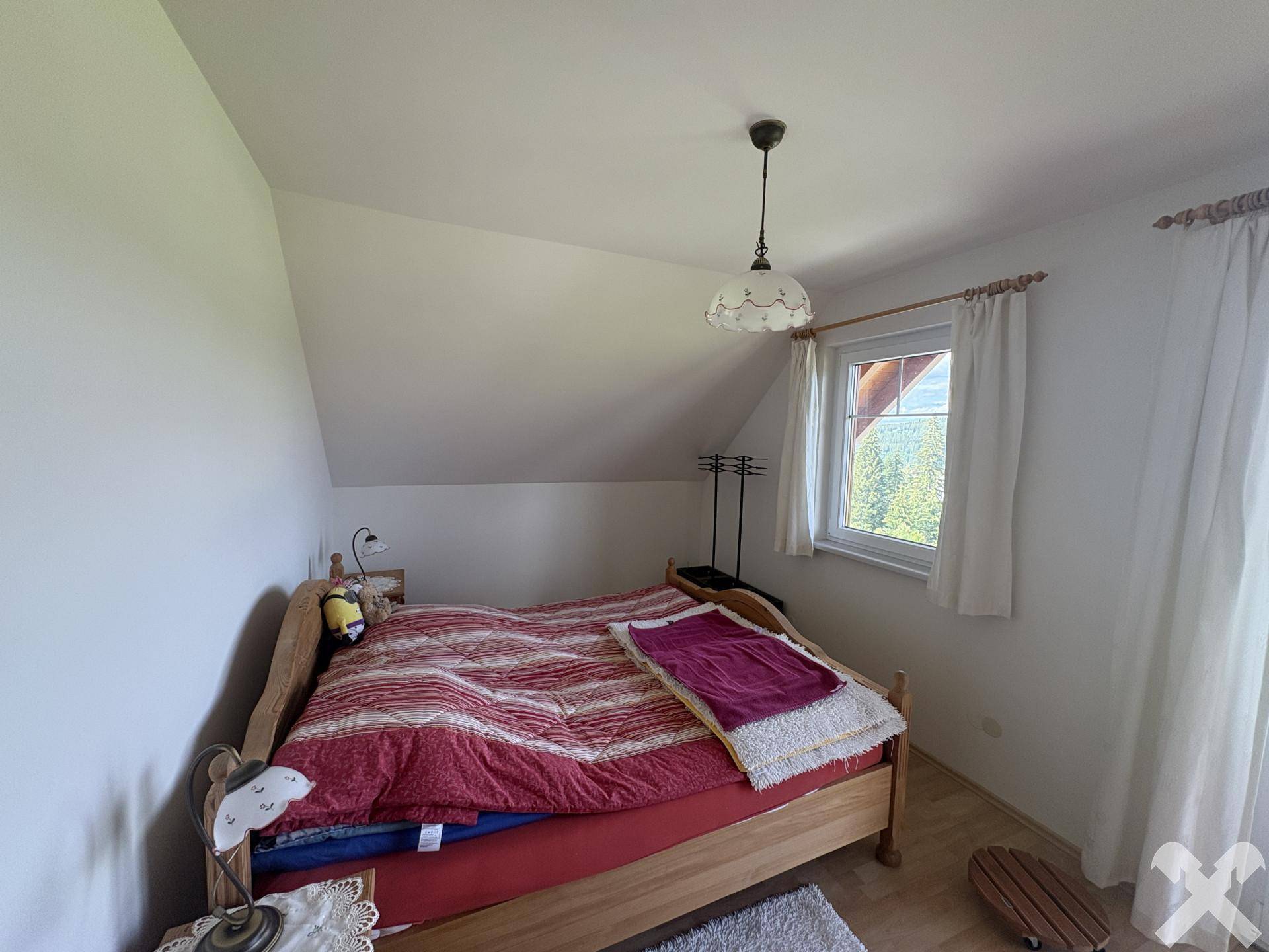 Schlafzimmer mit Doppelbett, Holzbettrahmen und Laminatboden unter Dachschräge.