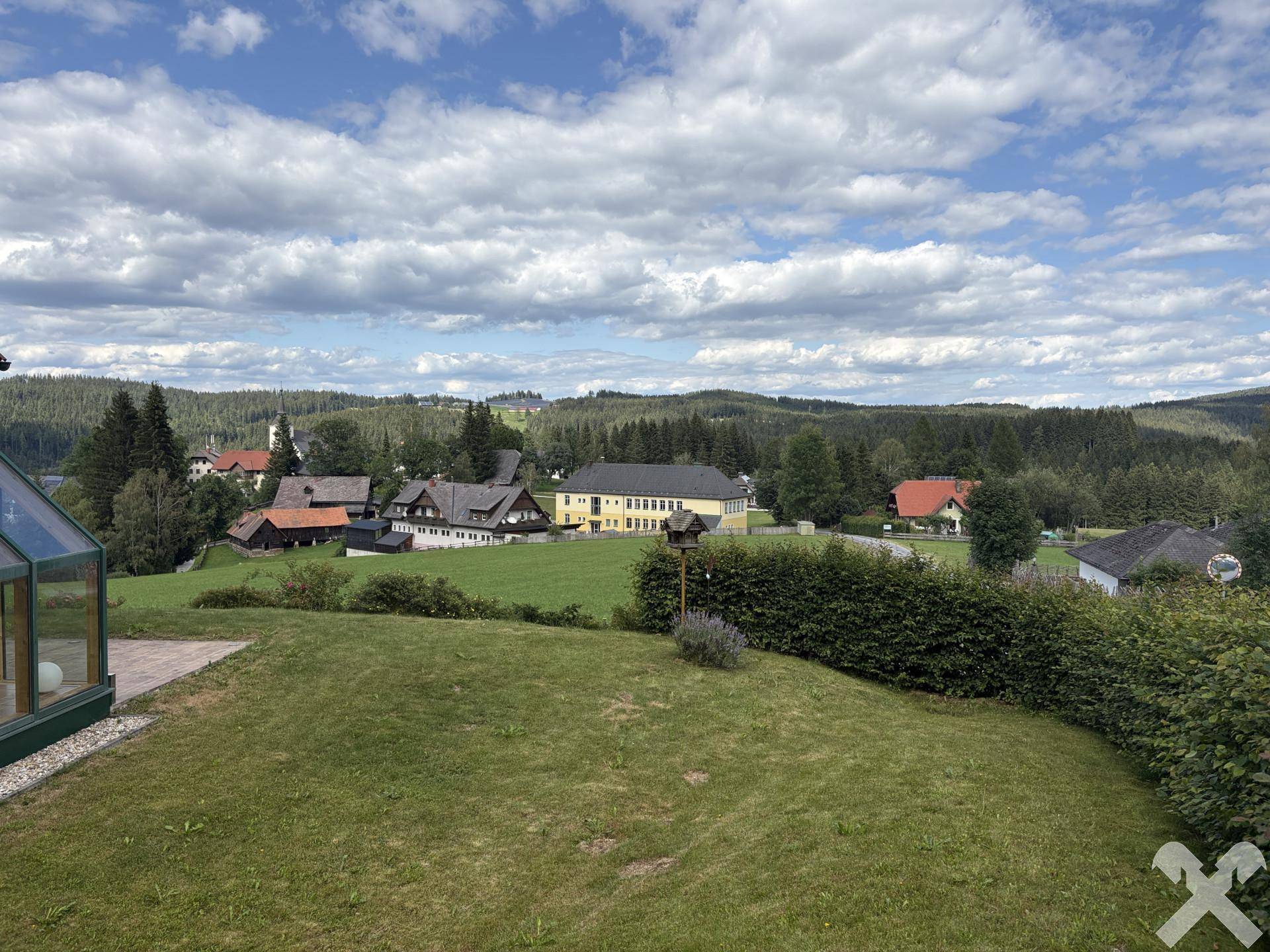 Weitläufiger Garten mit Rasenfläche und Hecke, bietet einen weiten Blick auf die umliegende Landschaft und ein kleines Dorf.