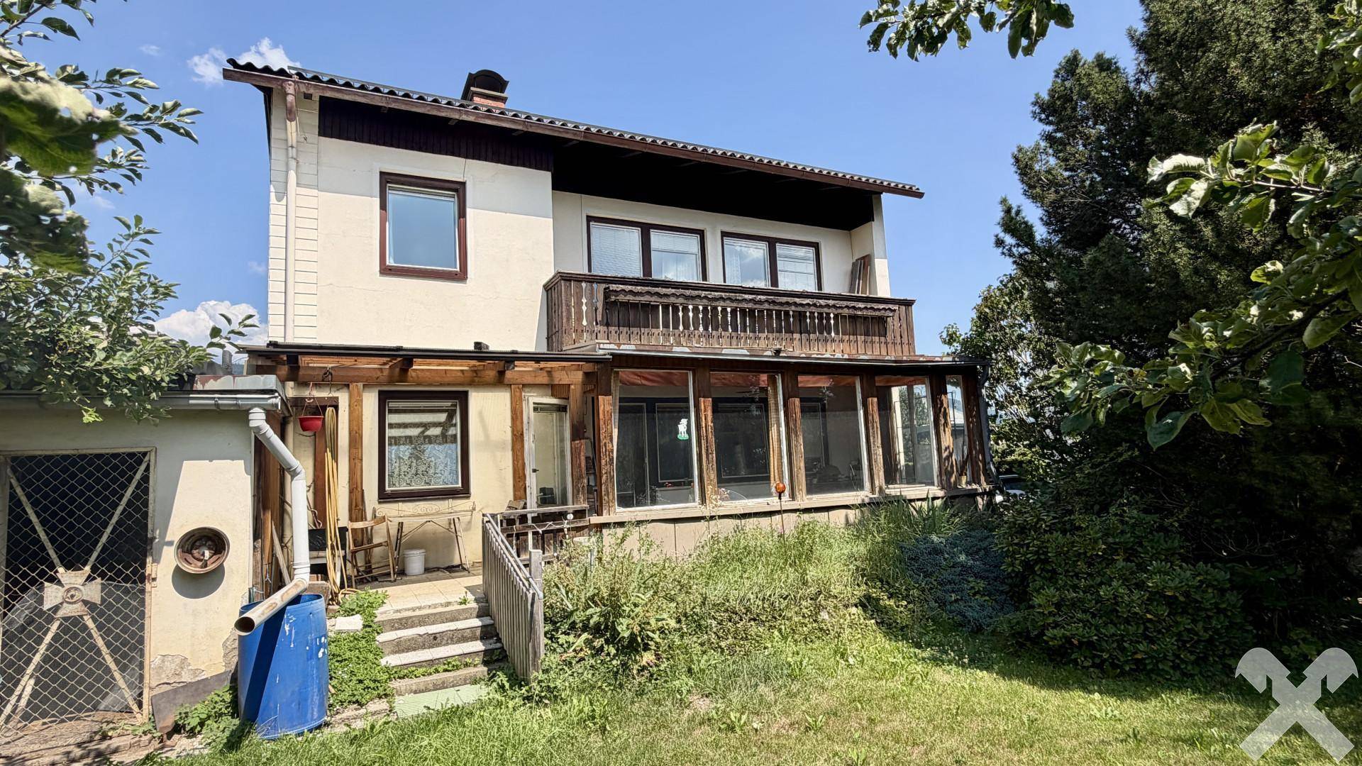 Rückseite des Hauses mit Garten, Balkon und Wintergarten, umgeben von viel Grün.
