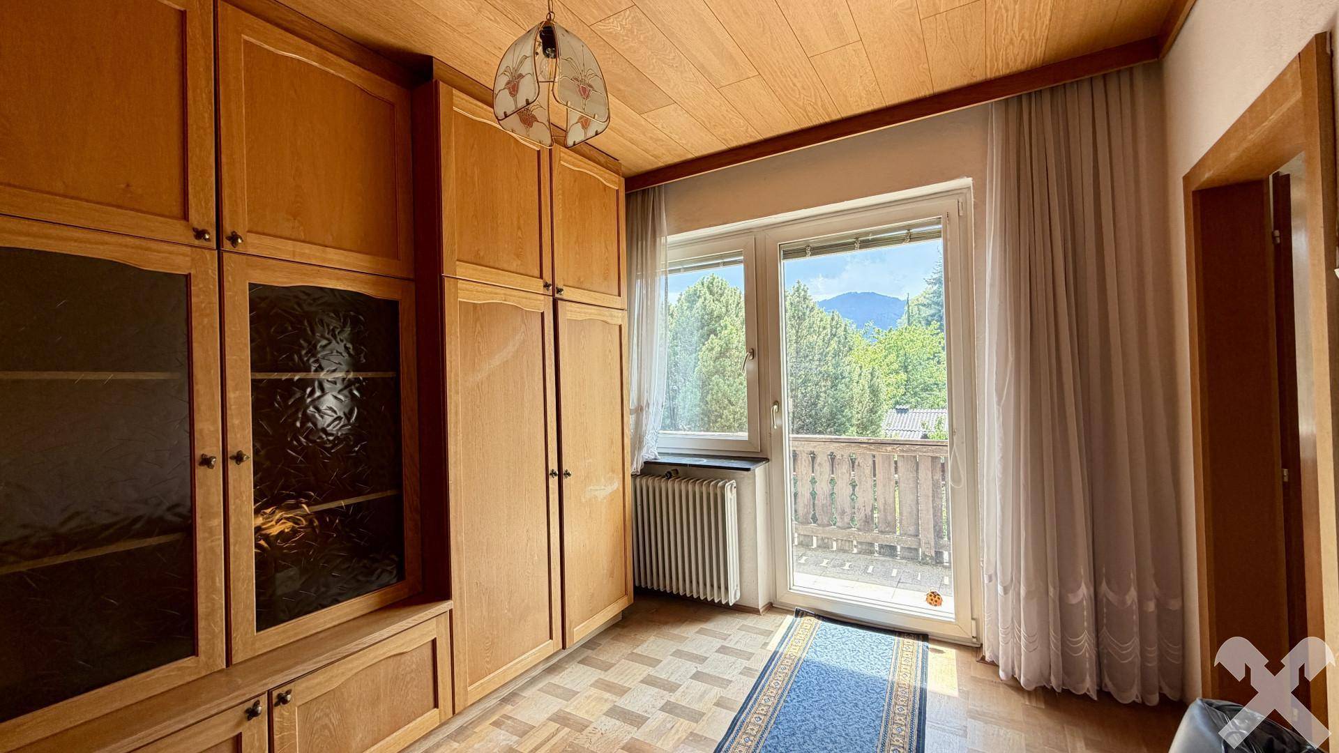 Schlafzimmer mit Einbauschränken, Holzboden und Zugang zu einem kleinen Balkon.