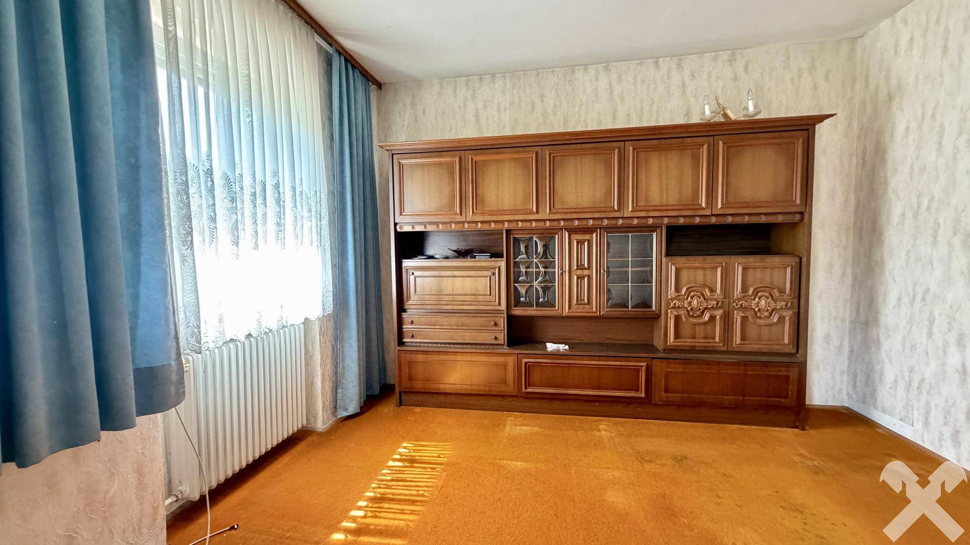 Wohnraum mit großem Holzschrank, Teppichboden und Fenster mit blauen Vorhängen.