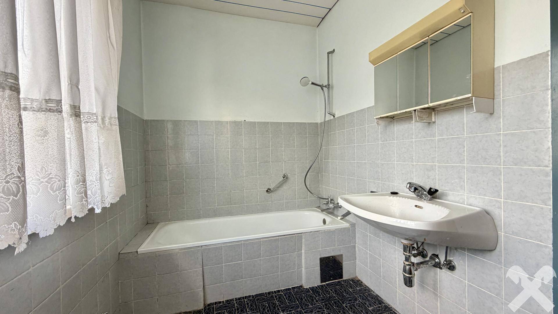 Badezimmer mit Badewanne, Waschbecken und grauen Fliesen im traditionellen Stil.
