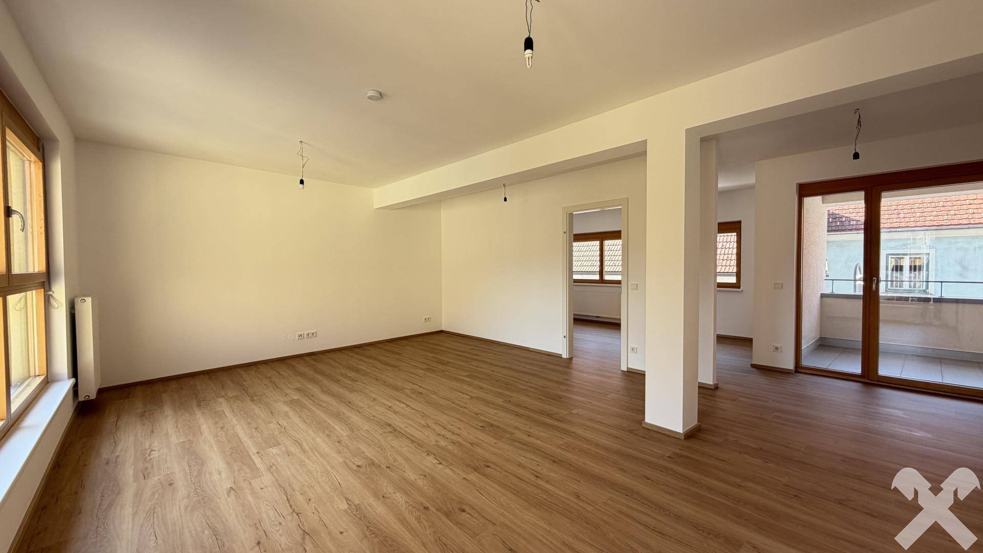 Geräumiger, leerer Wohnbereich mit Laminatboden, Zugang zum Balkon und viel Tageslicht.