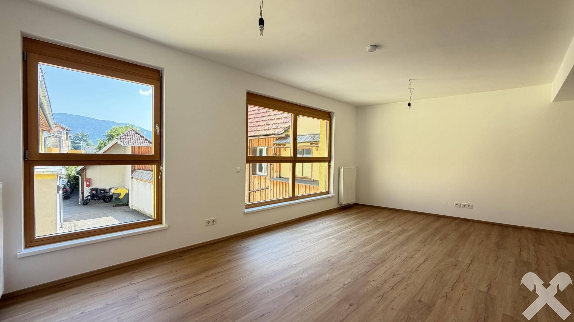 Heller, leerer Wohnraum mit großen Fenstern, Laminatboden und Bergblick.