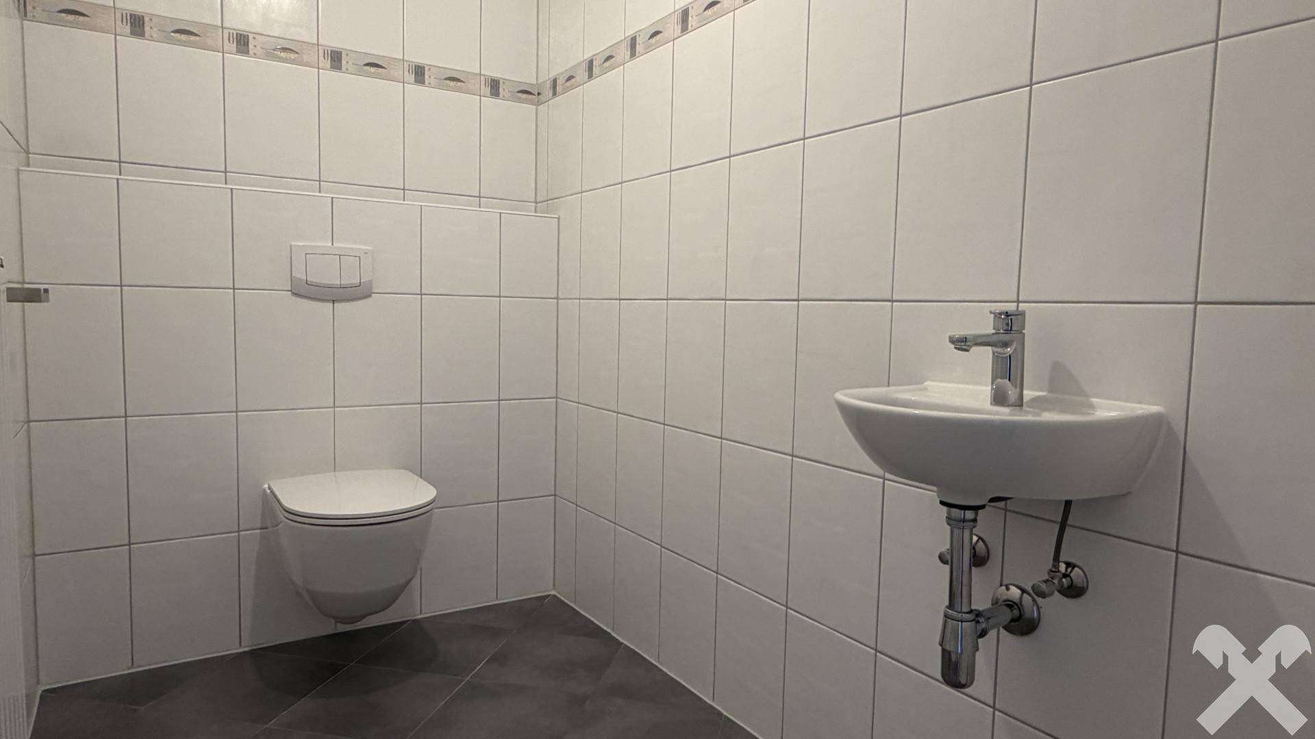 Separates Gäste-WC mit wandhängender Toilette, kleinem Waschbecken und weißen Fliesen.