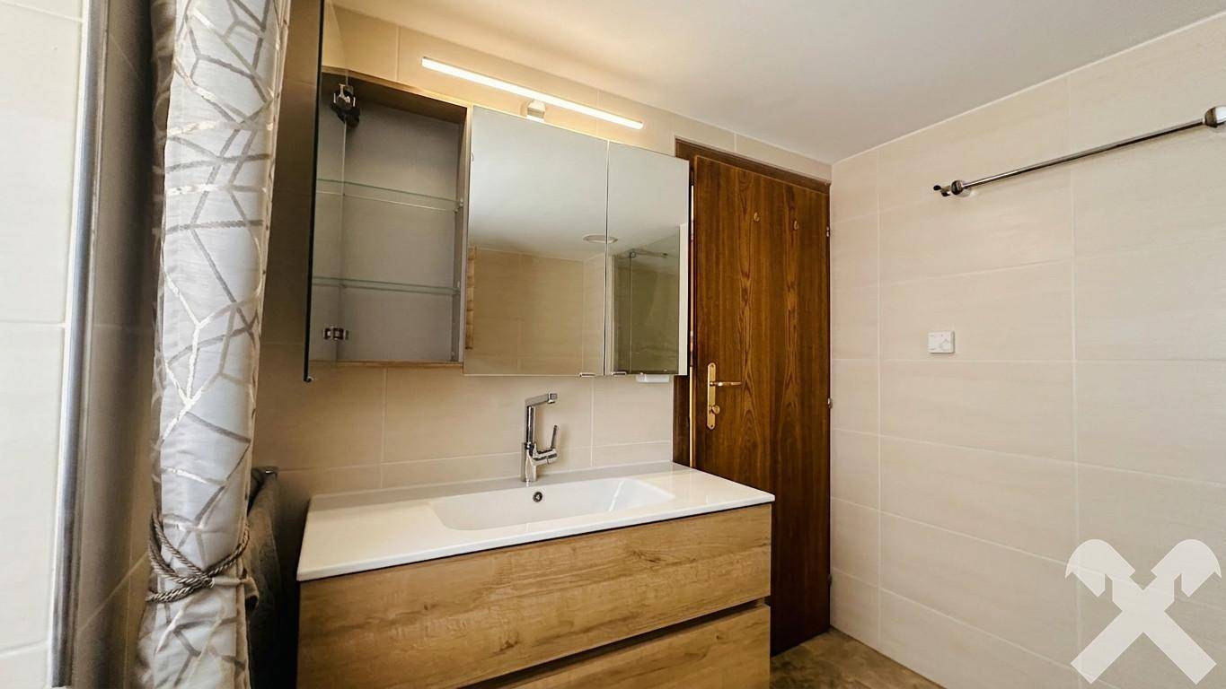 Modernisiertes Badezimmer mit Waschtisch, Spiegel und hellen Fliesen, bietet ausreichend Stauraum.