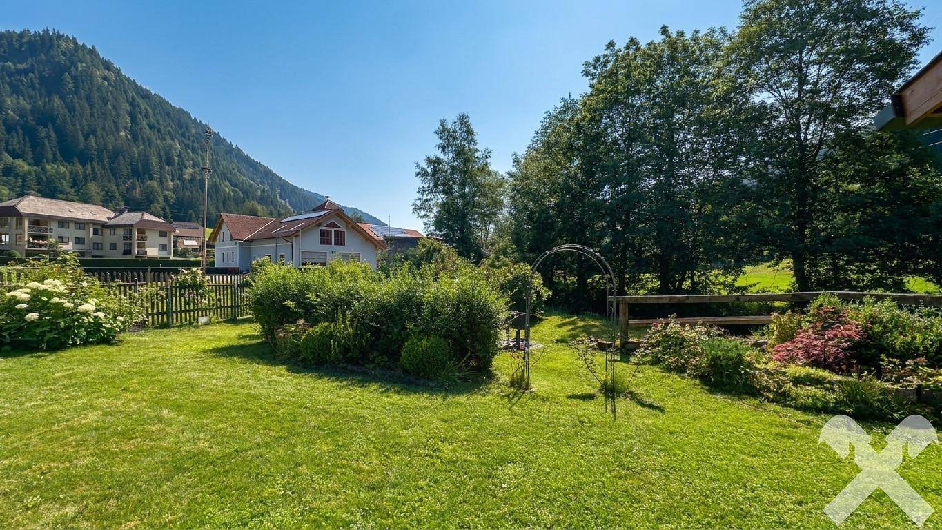 Großer, gepflegter Garten mit Rasen und Sträuchern, umgeben von ländlicher Idylle und Bergen.