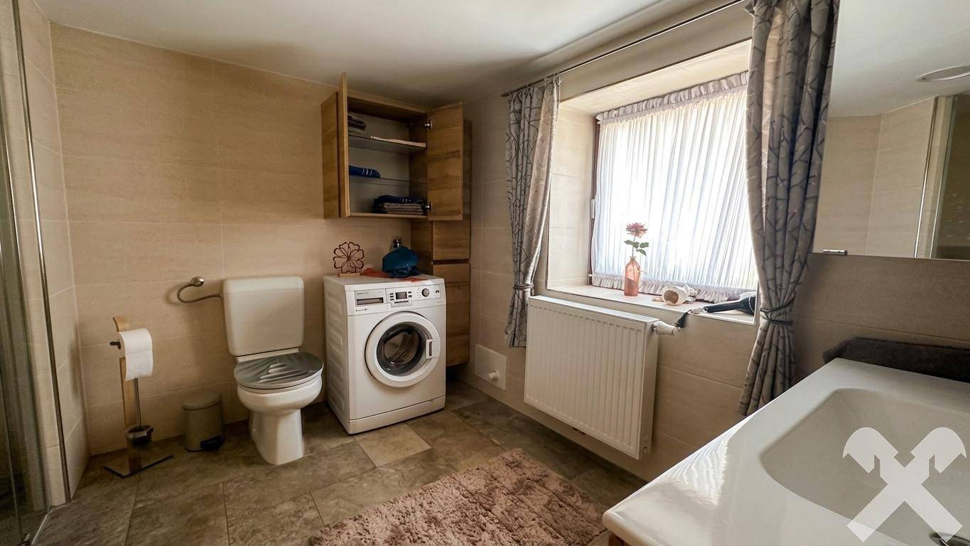Helles Badezimmer mit Fliesenboden, WC, Waschmaschine und Fenster für Tageslicht.