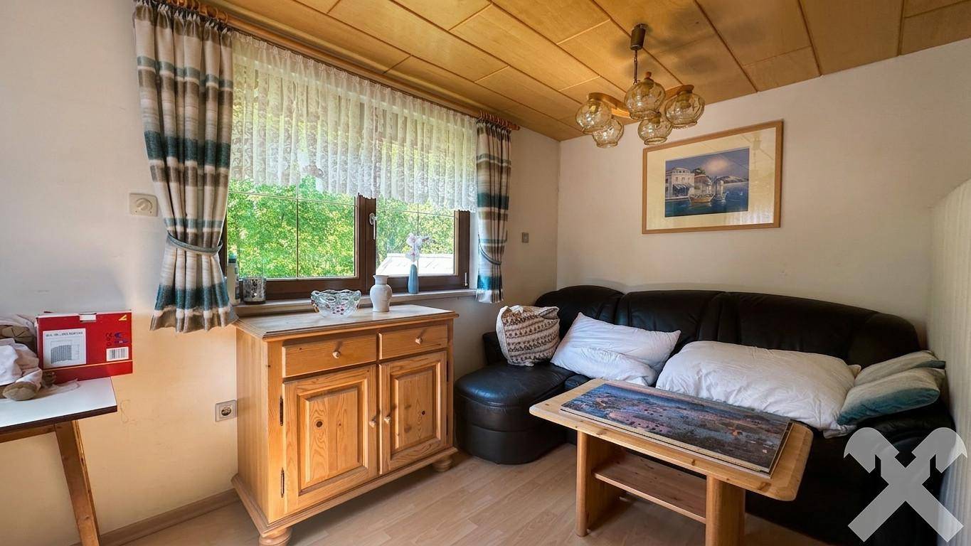 Helles Zimmer mit Sitzgelegenheit, Holzmöbeln und Fenster, ideal als Gäste- oder Arbeitszimmer.
