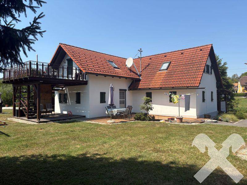 Rückseite des Hauses mit einer Holzterrasse, Gartenmöbeln und Wäscheleine im Grünen.