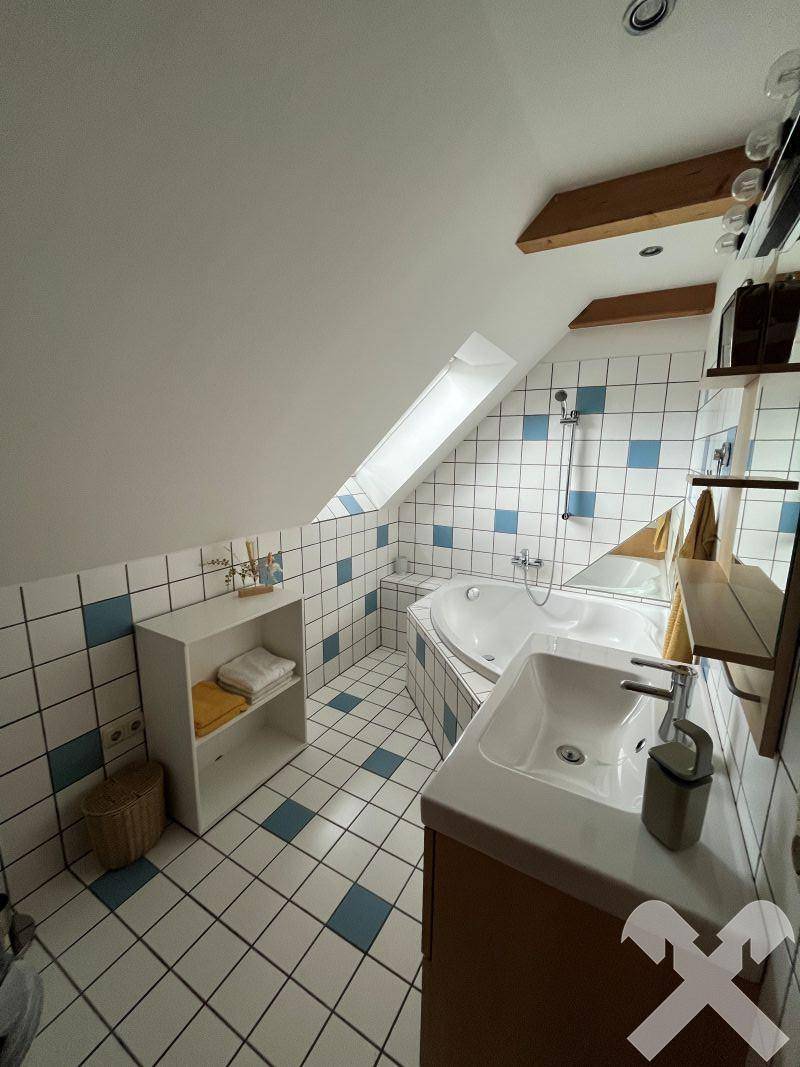 Dachgeschoss-Badezimmer mit Eckbadewanne, Waschbecken und blau-weiß karierten Fliesen.