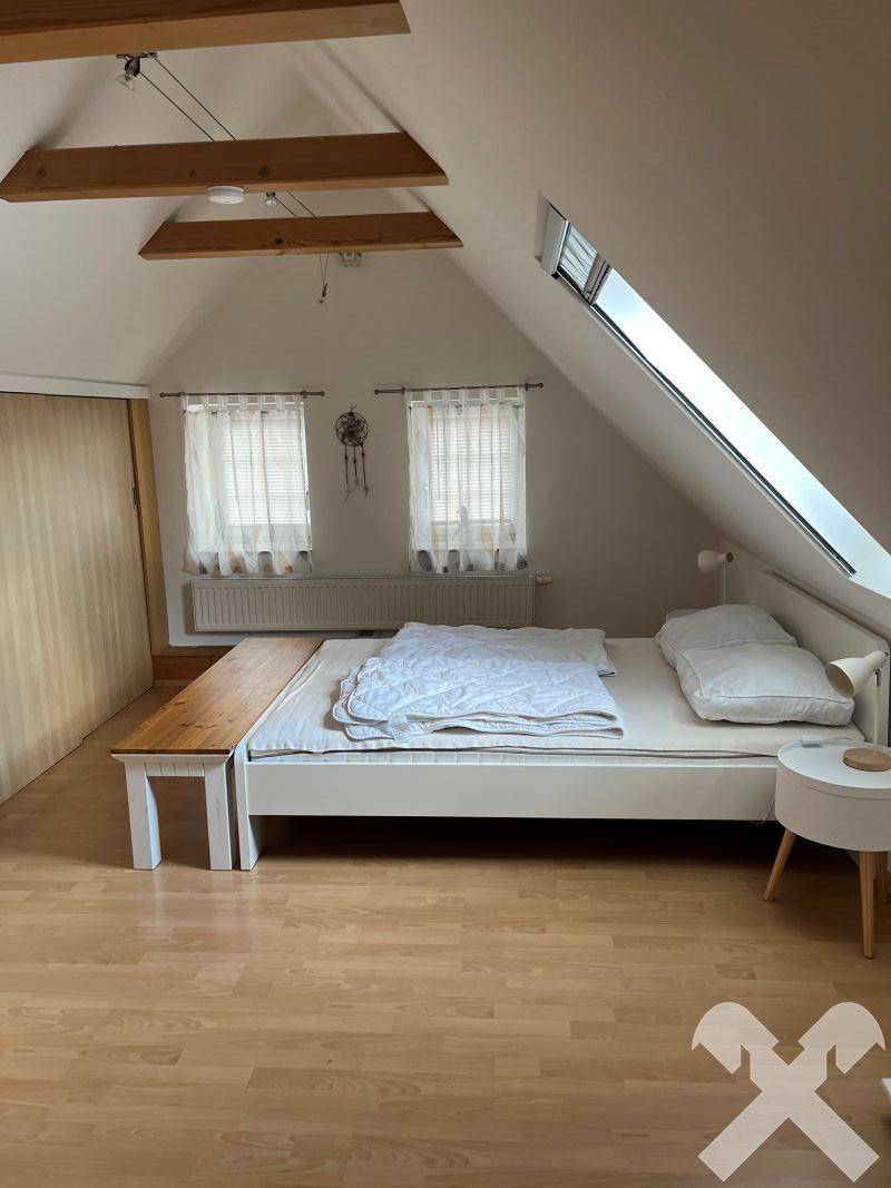 Helles Schlafzimmer im Dachgeschoss mit Dachschrägen, Holzboden und gemütlichem Bett.